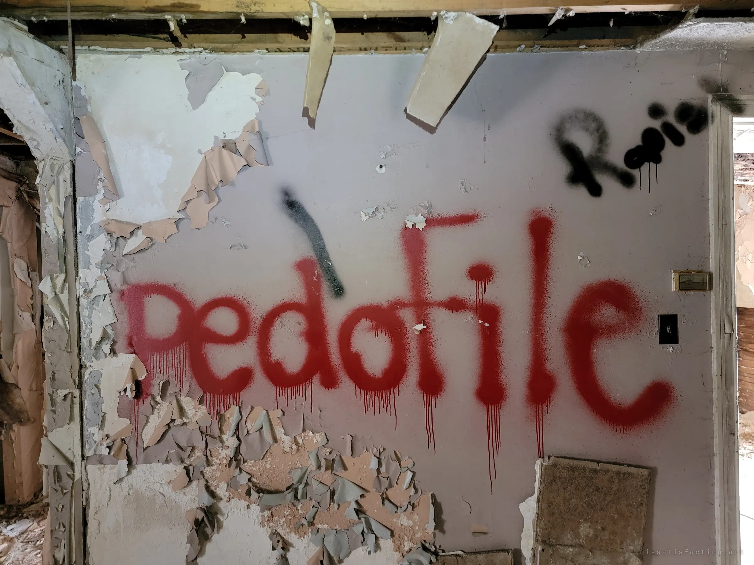 A peeling wall covered in large dripping red spray-painted letters accusing the former occupant, with more black graffiti above. The graffiti gives the house its grim reputation.