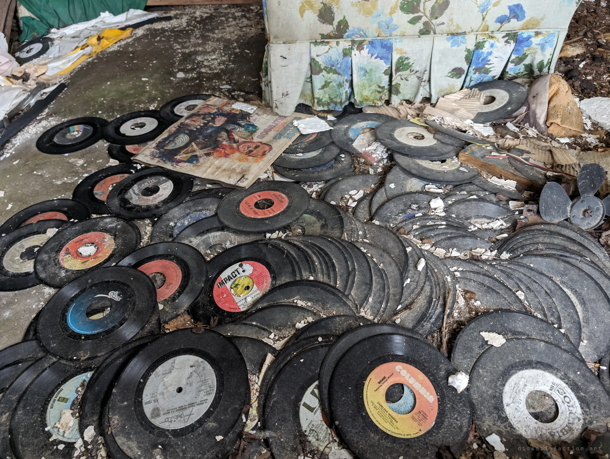 Dozens of dusty 45 rpm singles spread across the floor at the foot of the floral armchair, a faded record sleeve on top. A lost record collection slowly crumbling in the damp.