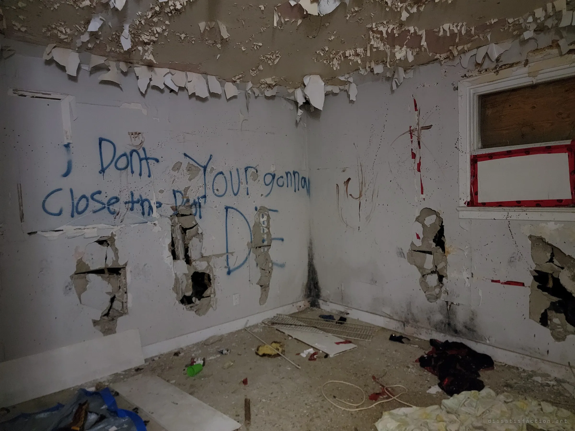 Blue spray paint across a peeling bedroom wall warns the reader to close the door or die. Punched-in drywall and scattered clothes give the room its menace.