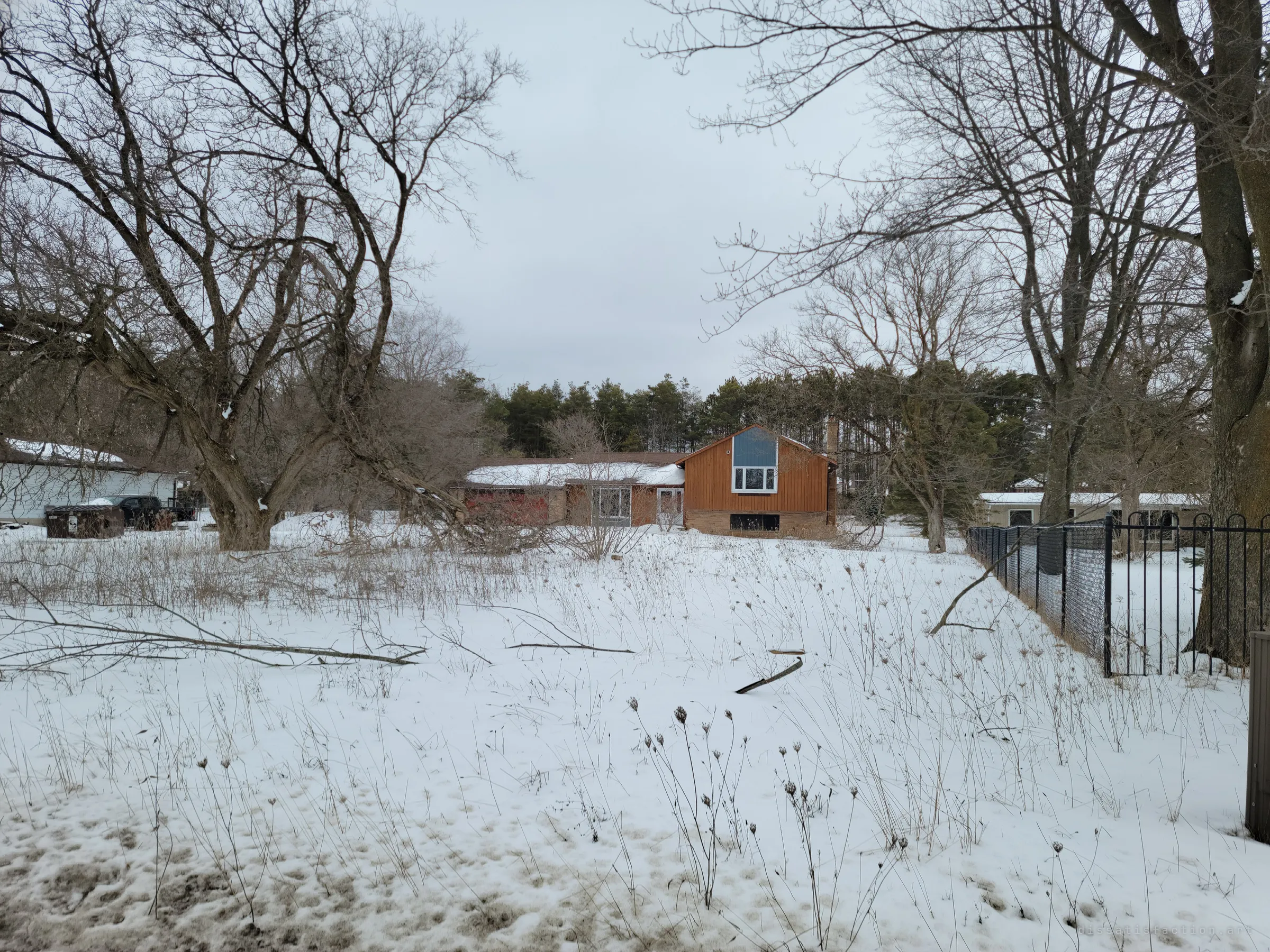 An abandoned split-level house with a tall gable window sits behind a snow-covered, overgrown yard under bare winter trees. It sets the scene: a family home left to the weeds.