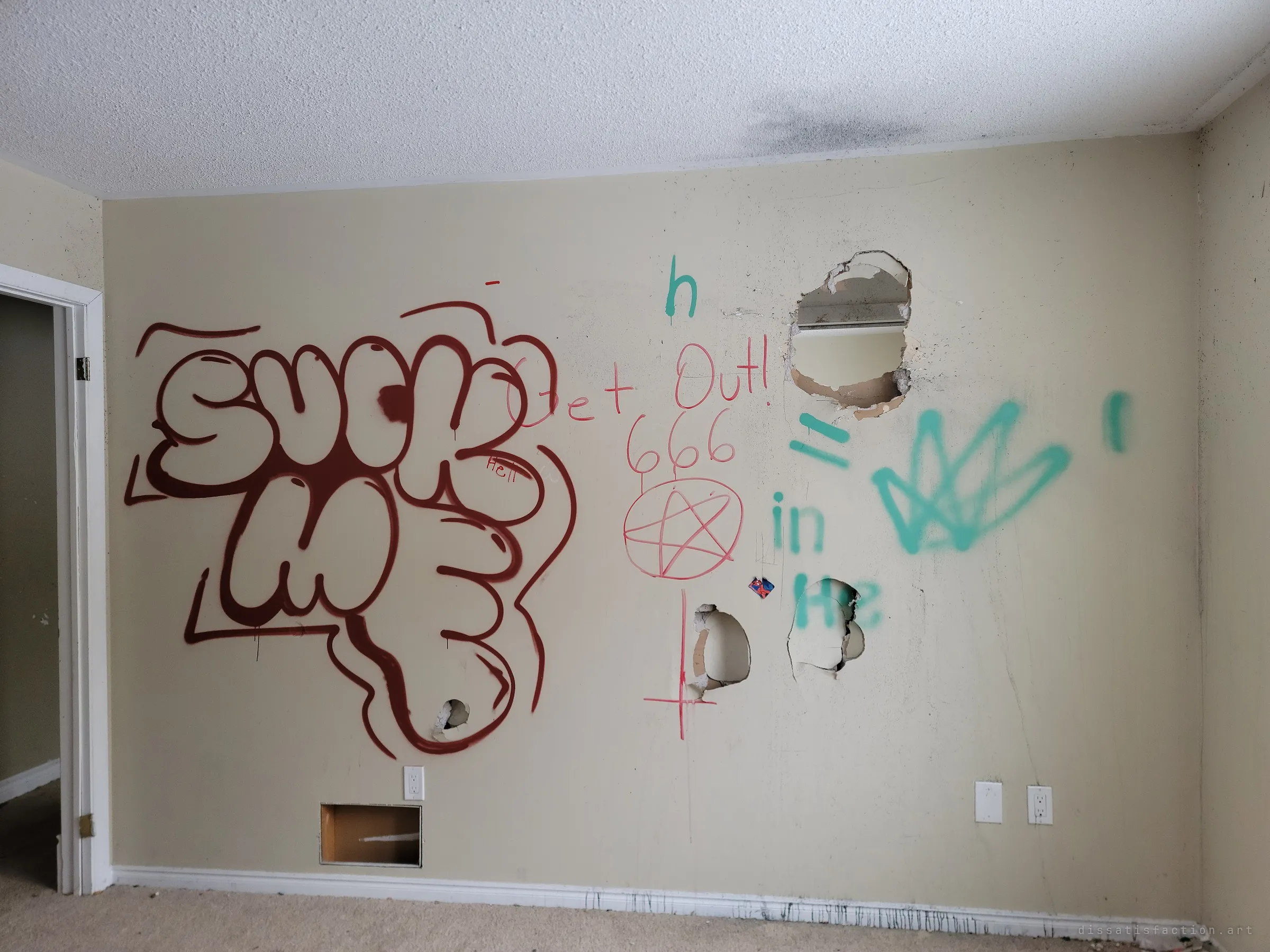 A bedroom wall tagged with a large bubble-letter throw-up, a red 'get out', 666 and a pentagram, plus green scrawl, the drywall smashed open in several places. Crude occult graffiti left by later visitors.