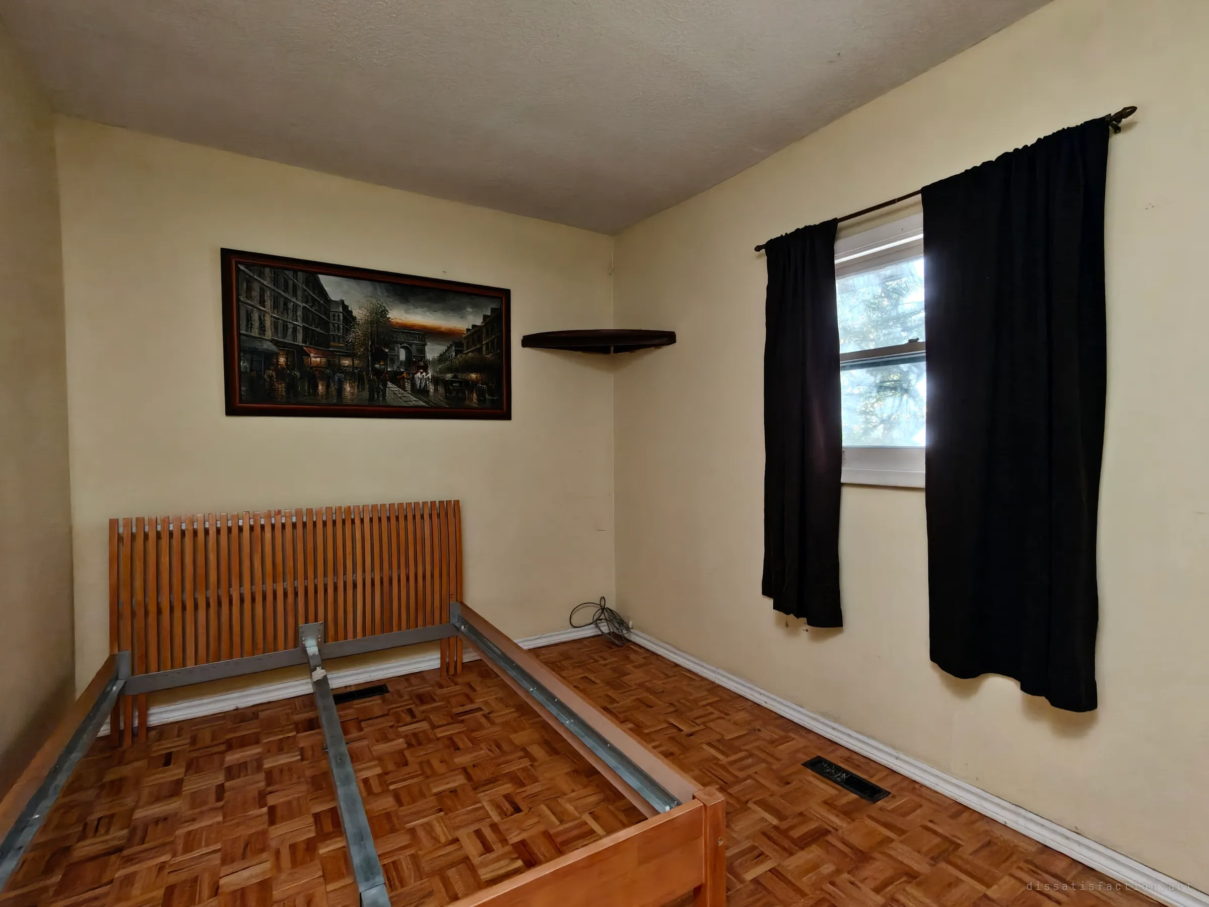 A bedroom with a slatted wooden bed frame on parquet flooring and a painting of a Paris street on the wall. Dark curtains frame a small window.