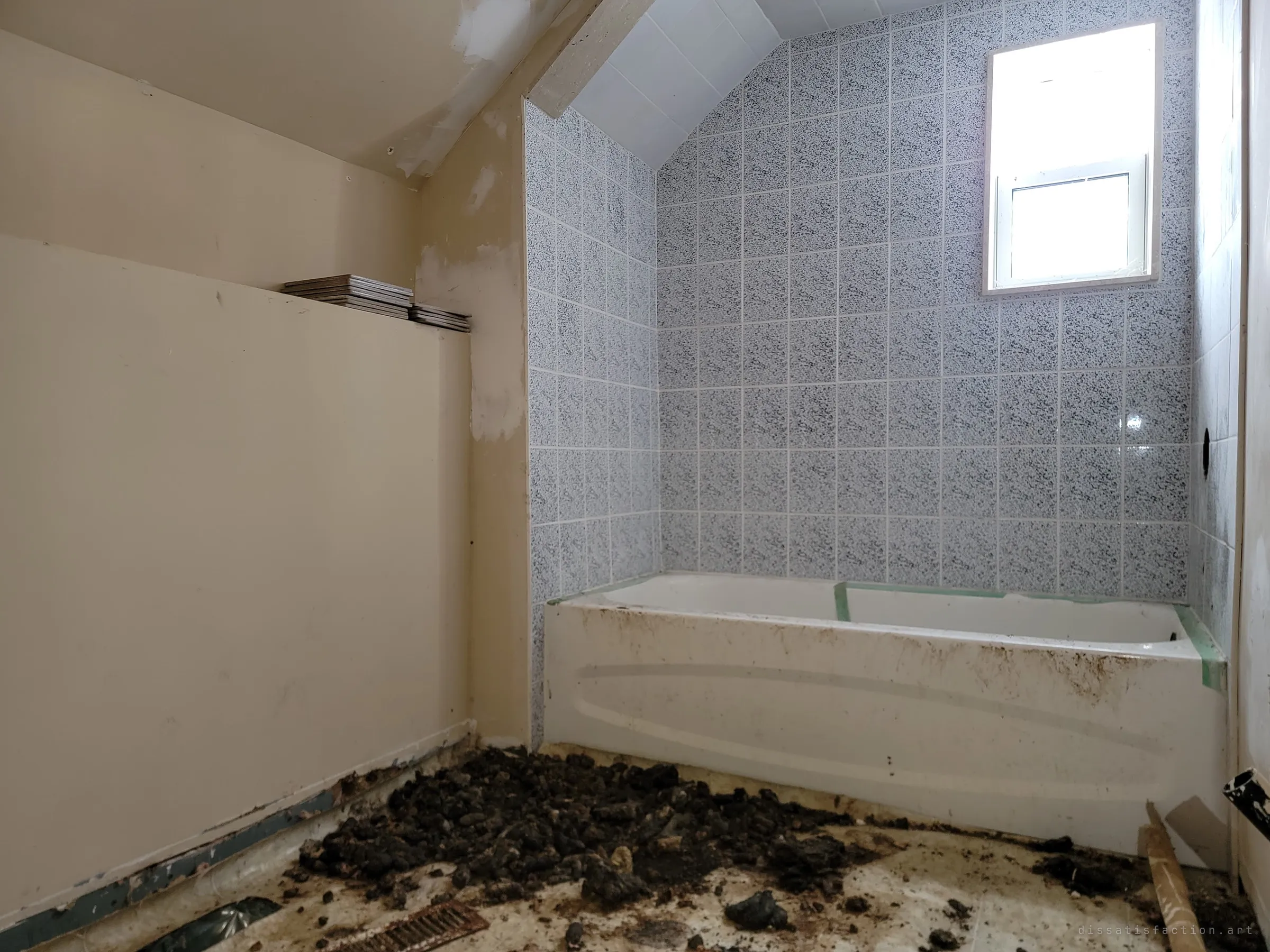 An attic bathroom with a speckled tile surround, a small bright window and a grimy, taped-up tub, its floor heaped with droppings and debris. A clean-looking room slowly taken over by animals.
