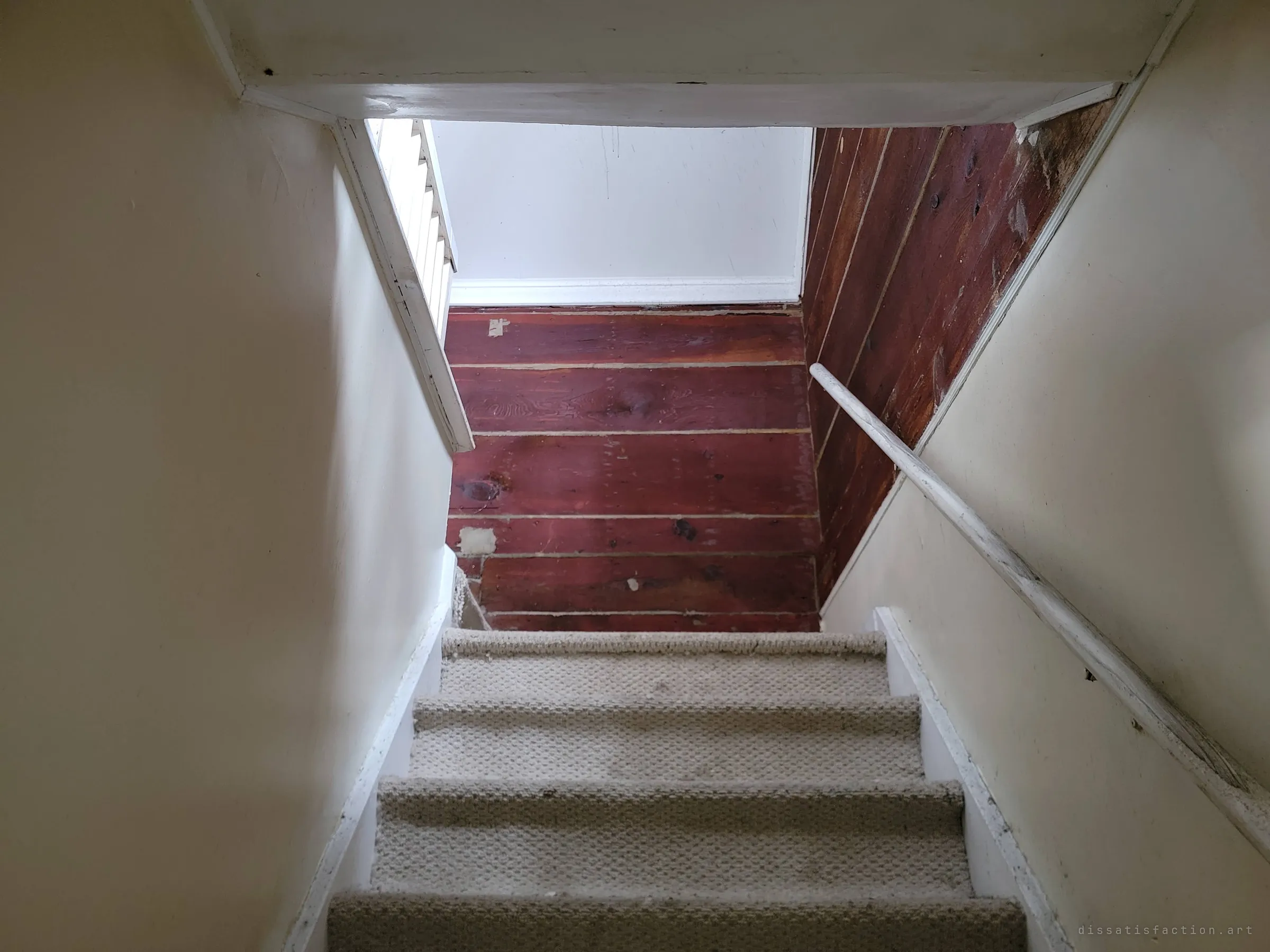 Looking up a narrow carpeted staircase toward a landing panelled in dark red wood boards. The worn treads lead to the upper floor.
