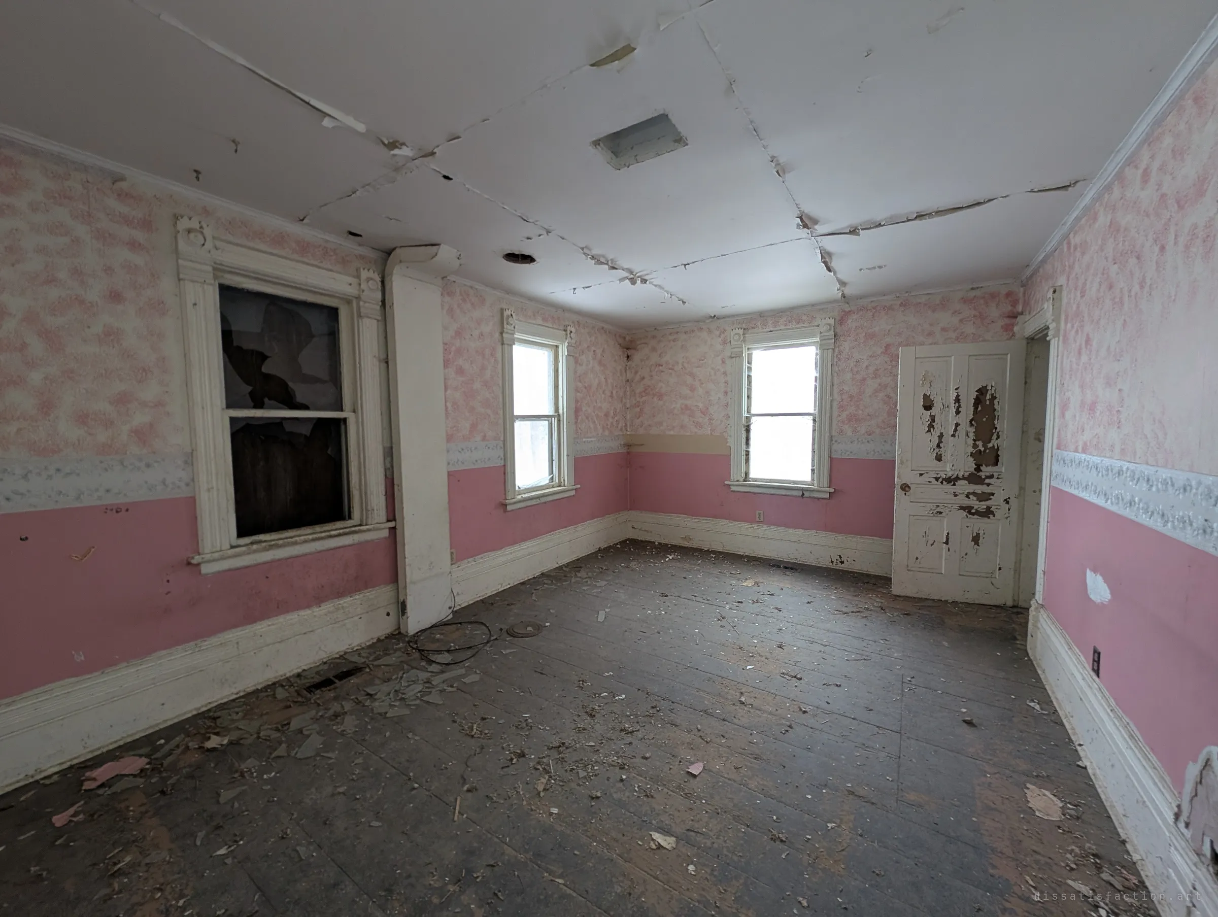 A pink bedroom with sponge-painted walls and a floral border, the ceiling boards splitting apart and glass from a broken window on the floor. Soft winter light comes through the far windows.
