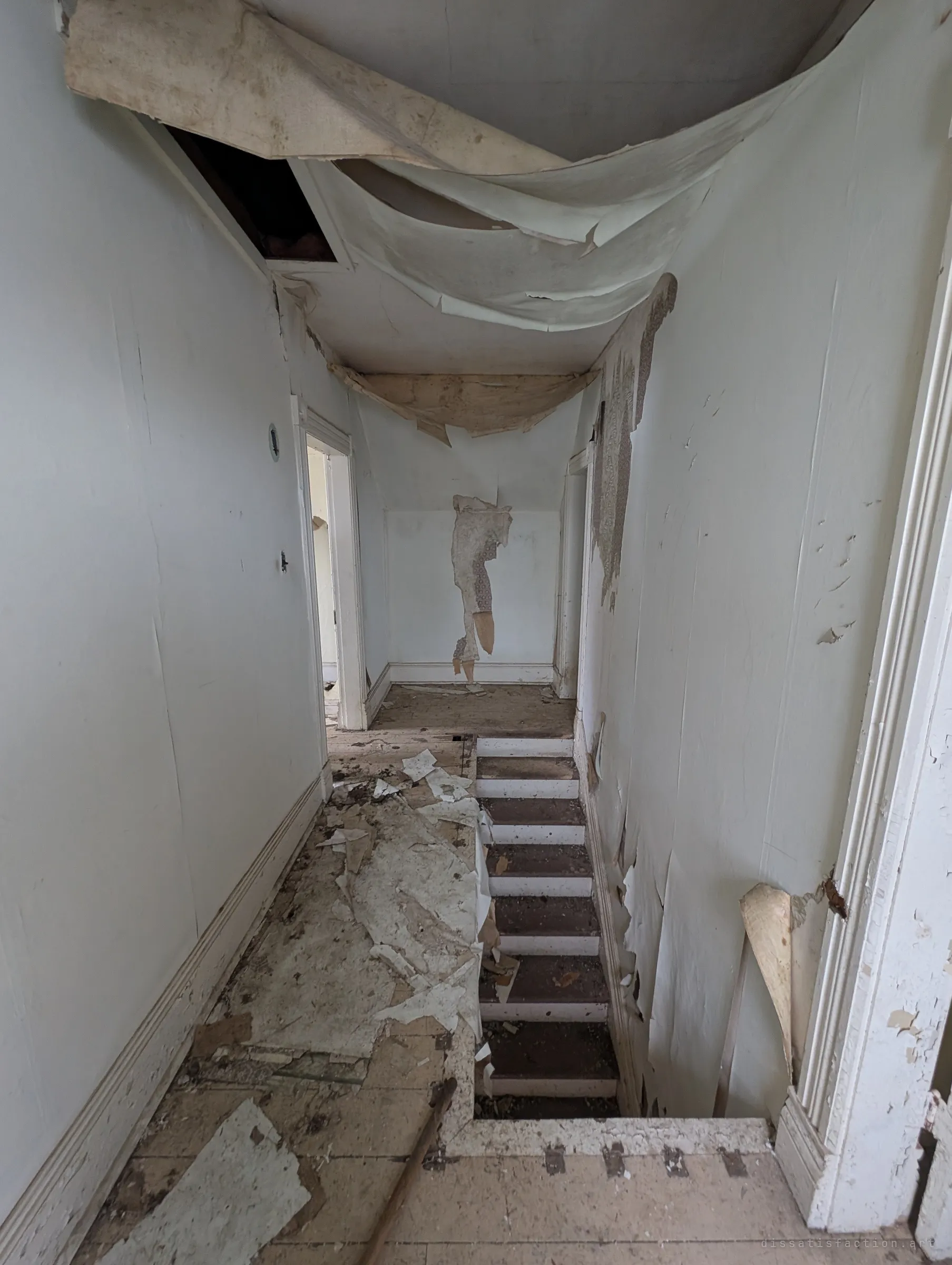 The upstairs hallway, with wallpaper sagging in great sheets from the ceiling and piled on the floor beside the top of the staircase.
