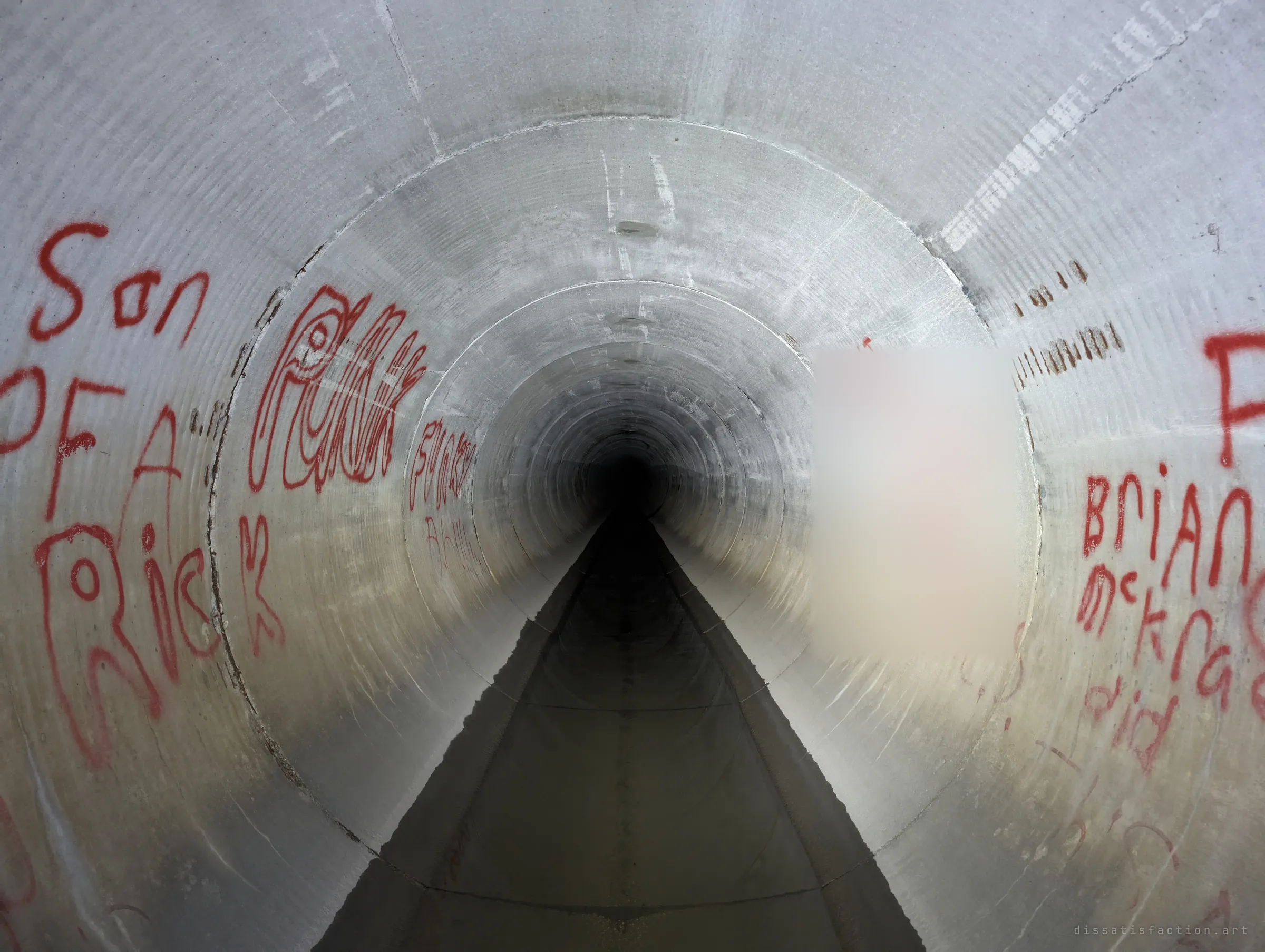 A straight concrete pipe with a narrow channel in its invert stretches into black, its walls tagged with red spray paint. The perfect symmetry pulls the eye to the vanishing point.