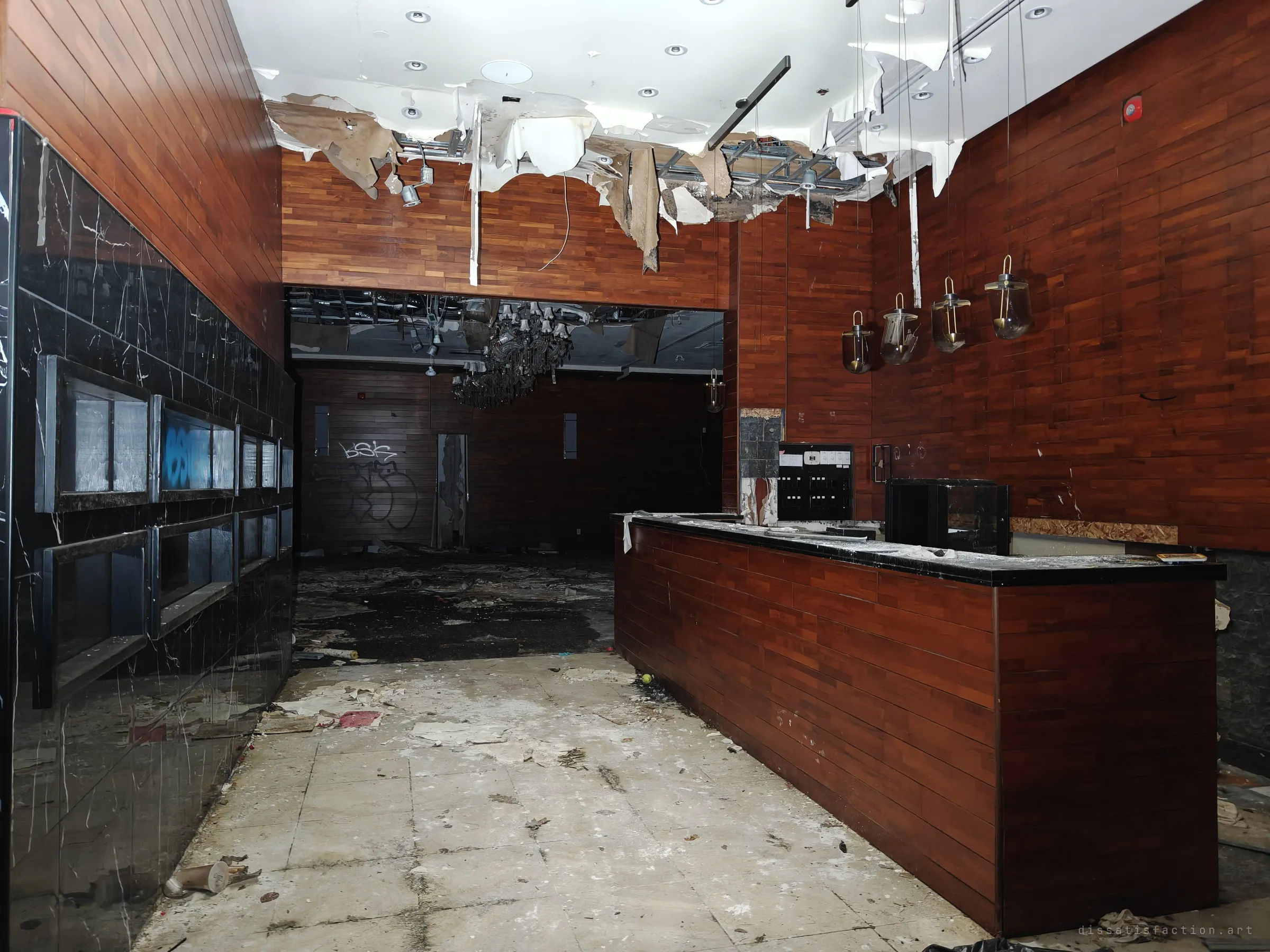 A lobby bar clad in red wood panels with a black marble wall at left. Hanging ceiling sheets drip over the counter, and graffiti marks the dark room beyond.