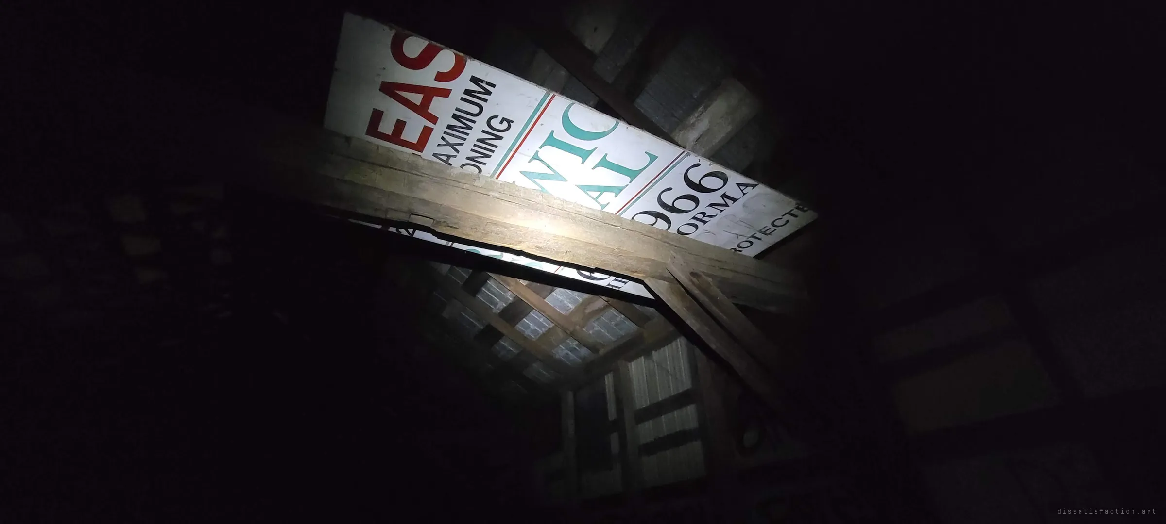 A flashlight picks out an old lease sign wedged into the rafters above a heavy wooden beam, its big red and teal letters cut off at odd angles. A leftover from when someone still hoped to rent the place.