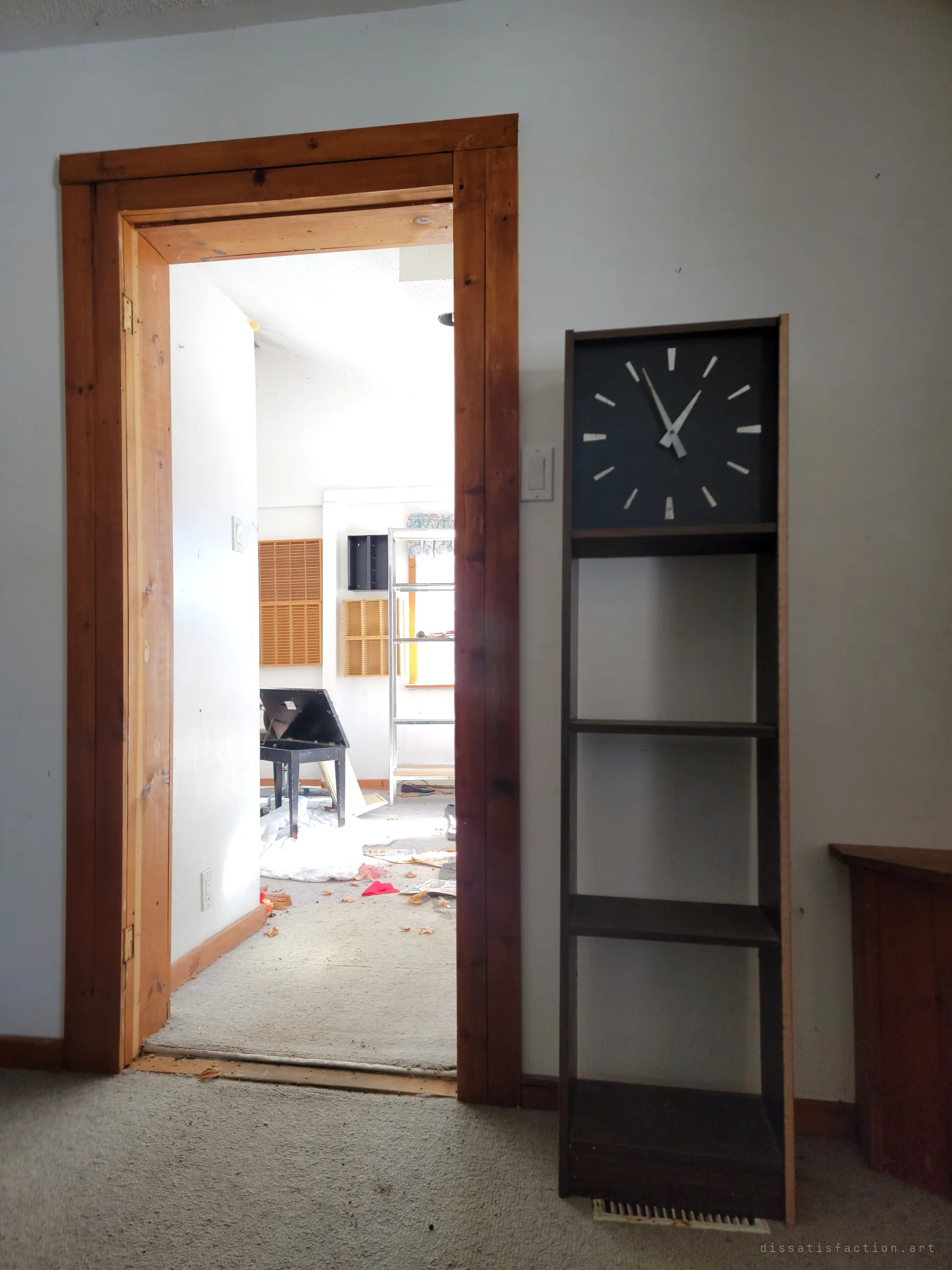 A rough pine doorframe beside a tall bookcase clock, opening onto a bright room with an open piano bench and scattered papers on the carpet. Time on the clock face has stopped.