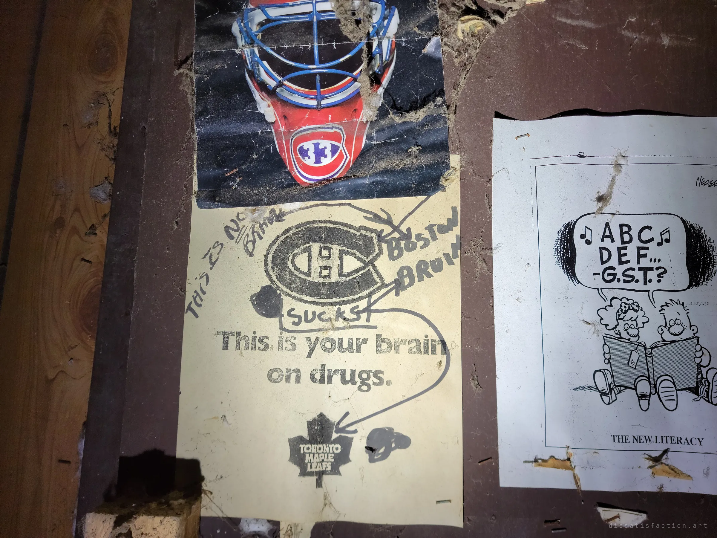 Old hockey posters on the break-room door, one defaced with scribbled team insults, next to a photocopied cartoon about sales tax. Decades-old workplace humour still pinned where it was left.