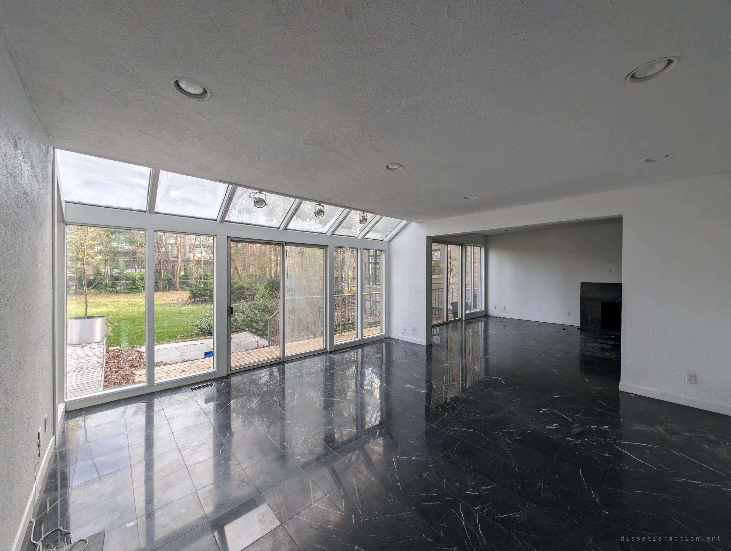 A sunroom-style living space with a sloped glass roof and a floor of polished black marble that mirrors the windows. The empty yard outside makes the room feel even more vacant.