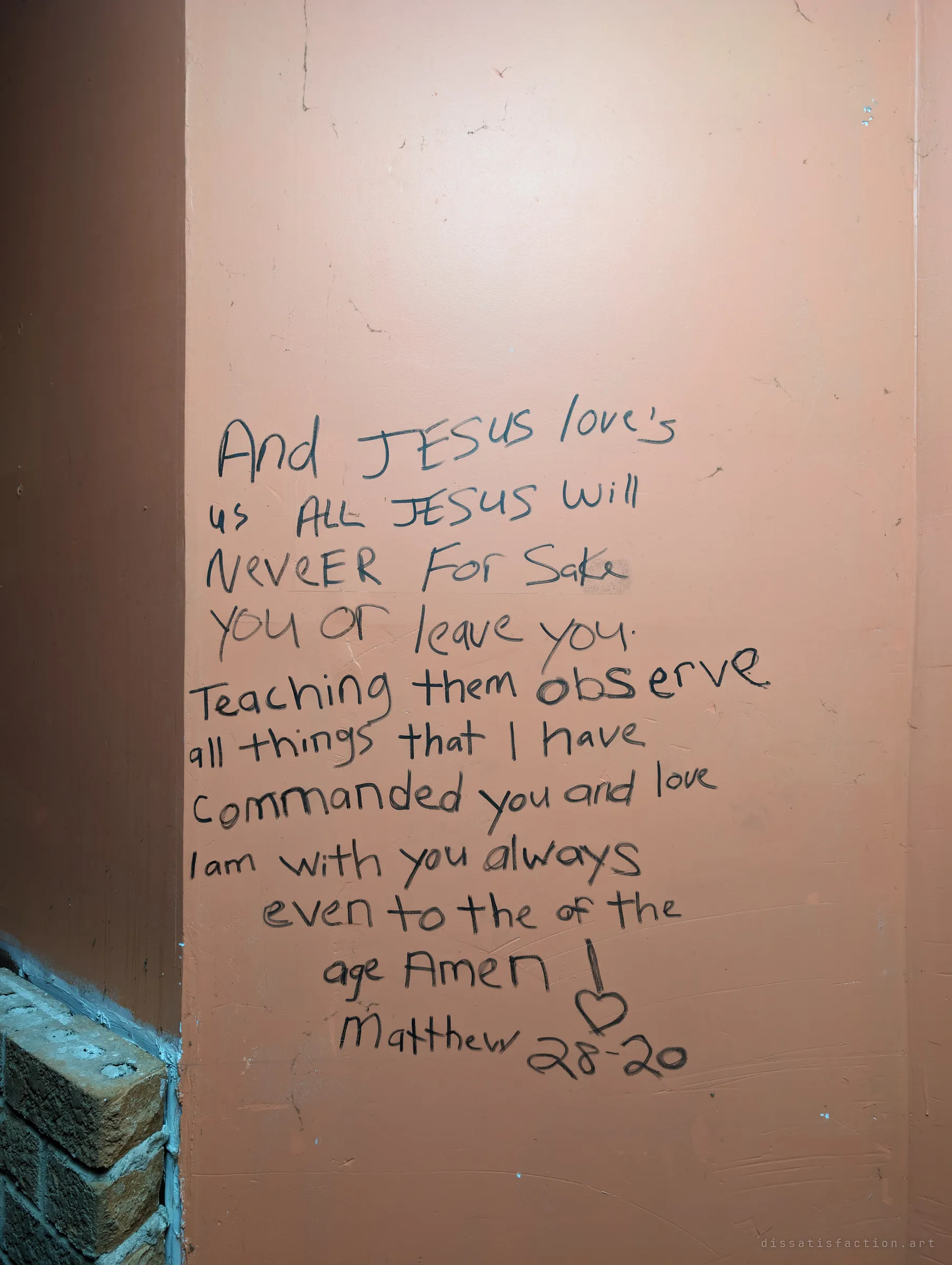 A hand-written Bible verse in black marker on a peach wall beside a brick corner. It is one of the many messages left throughout the house.