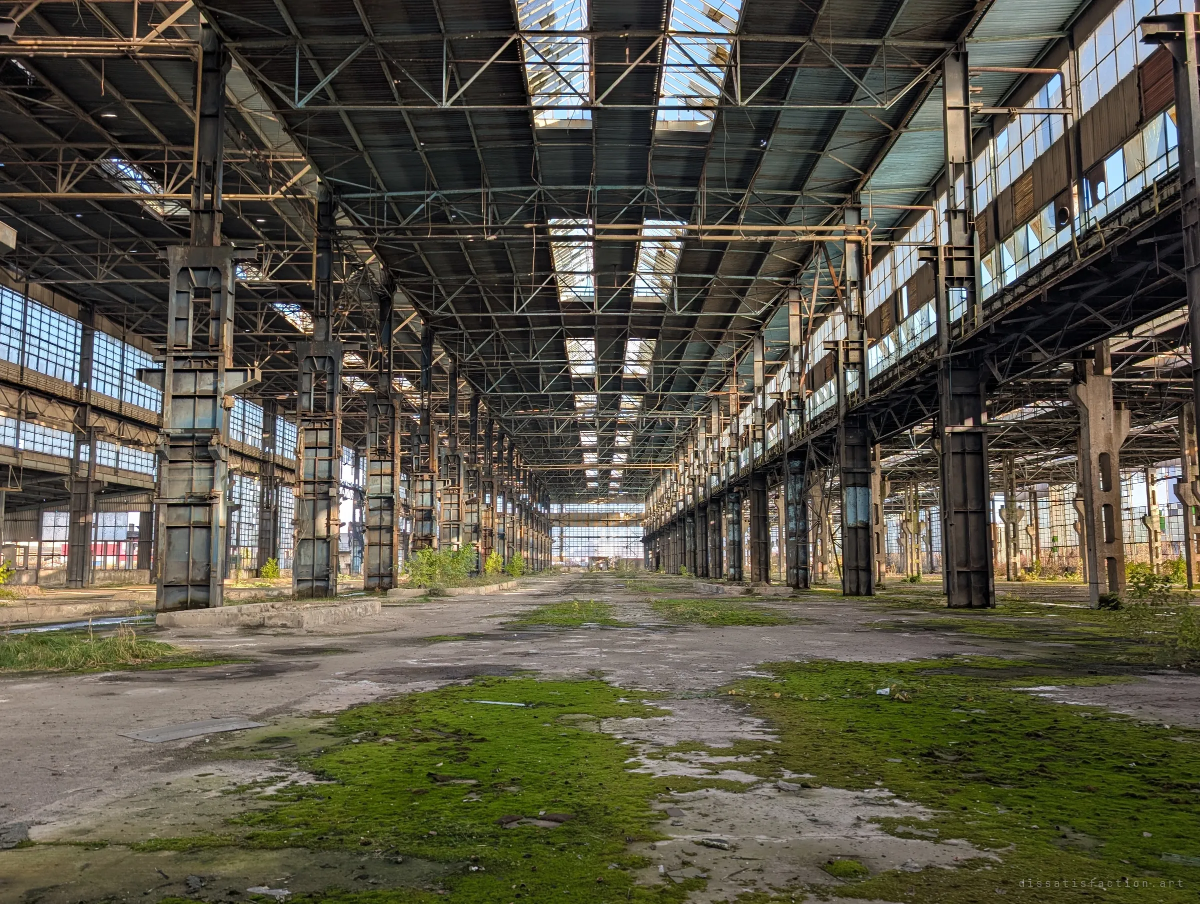 Symmetrical view down the central aisle of the hall, rows of riveted columns and skylights converging over a moss-covered floor.
