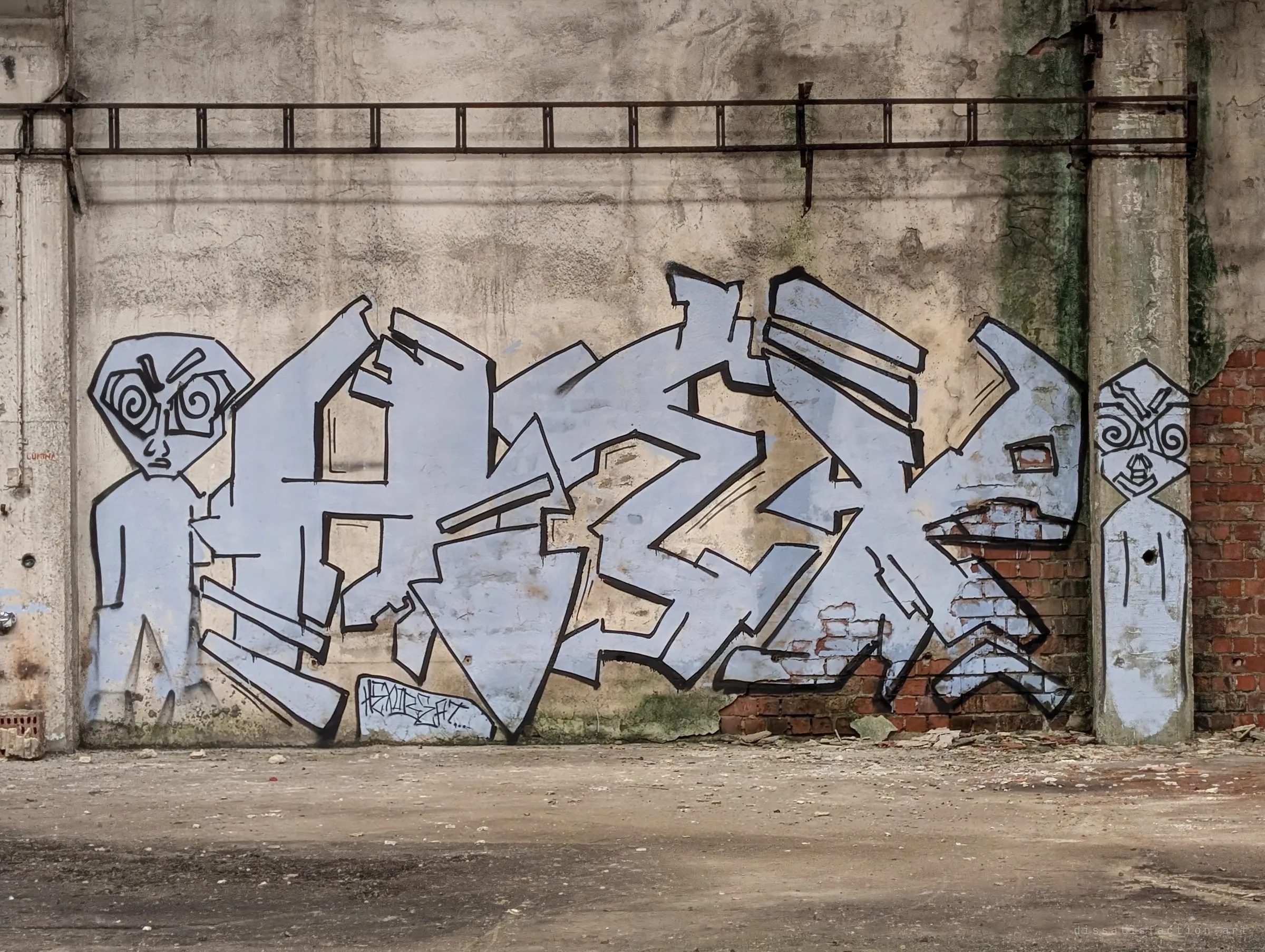 A pale lavender graffiti piece flanked by two spiral-eyed alien figures covers a weathered wall where the plaster has fallen away to bare brick. A rusted rail runs along the wall above it.