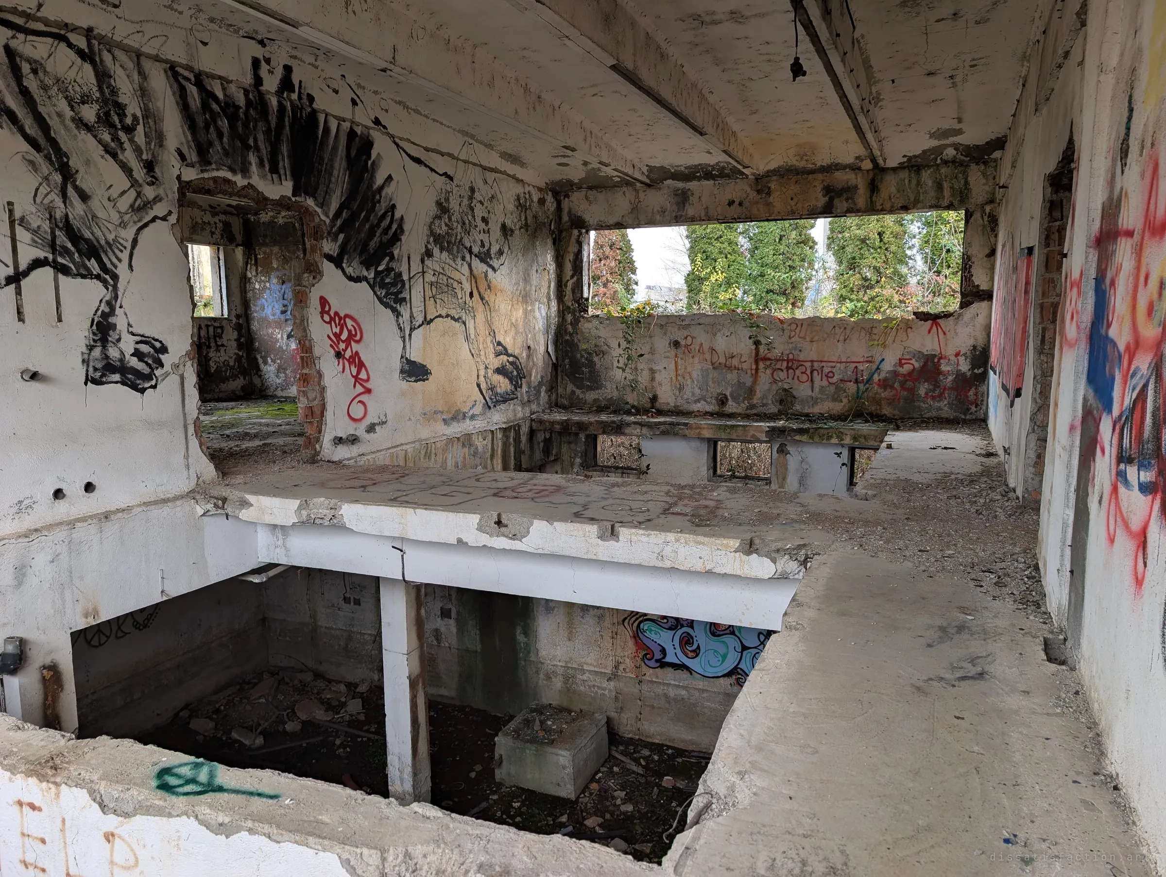 A split-level room with a large charcoal mural of clawed creatures, its floor broken open onto the flooded level below and trees pushing in at the window.