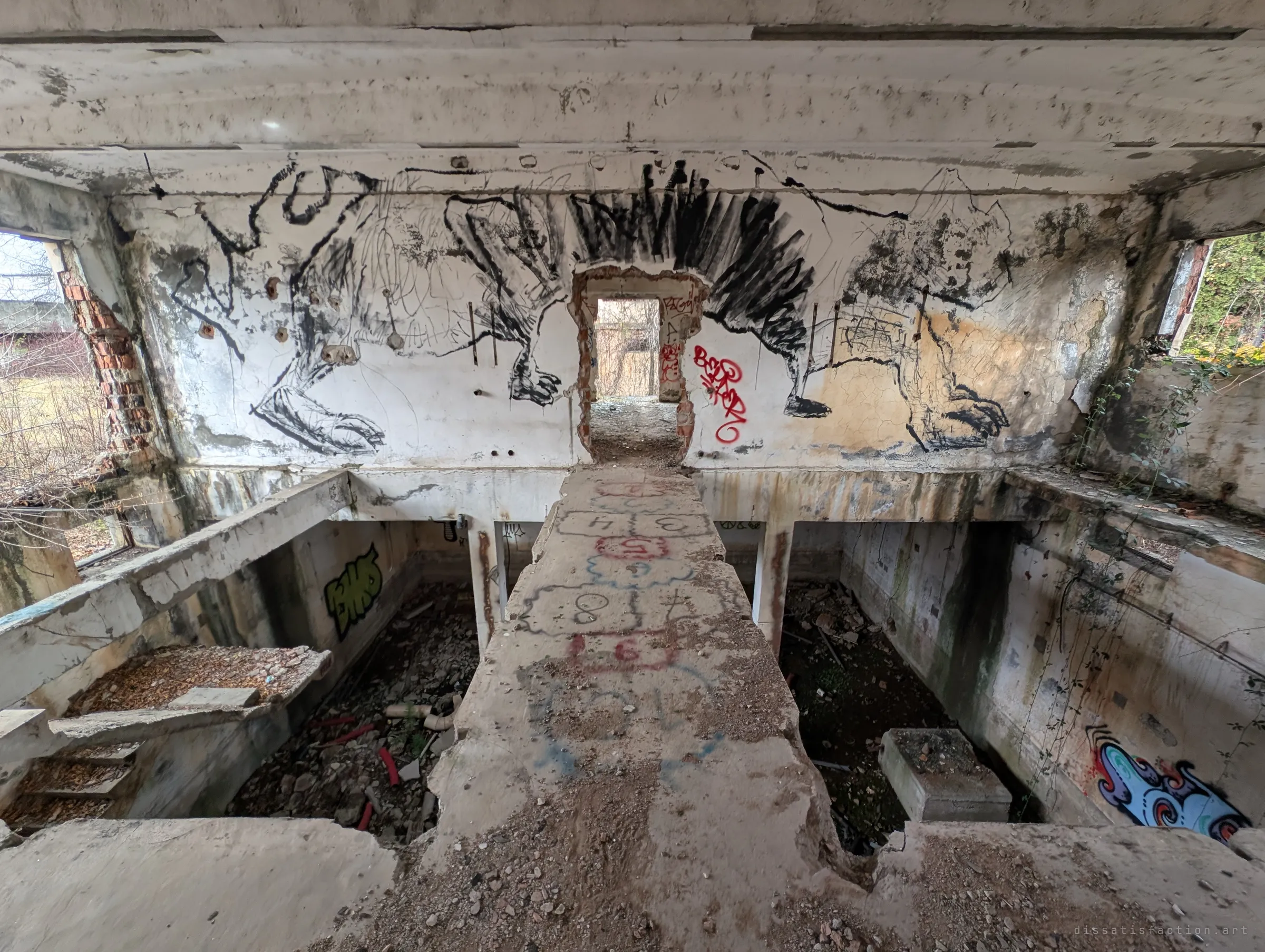 A narrow concrete bridge with a hopscotch grid chalked on it crosses over two collapsed pits toward a doorway framed by a sprawling black mural of beasts.