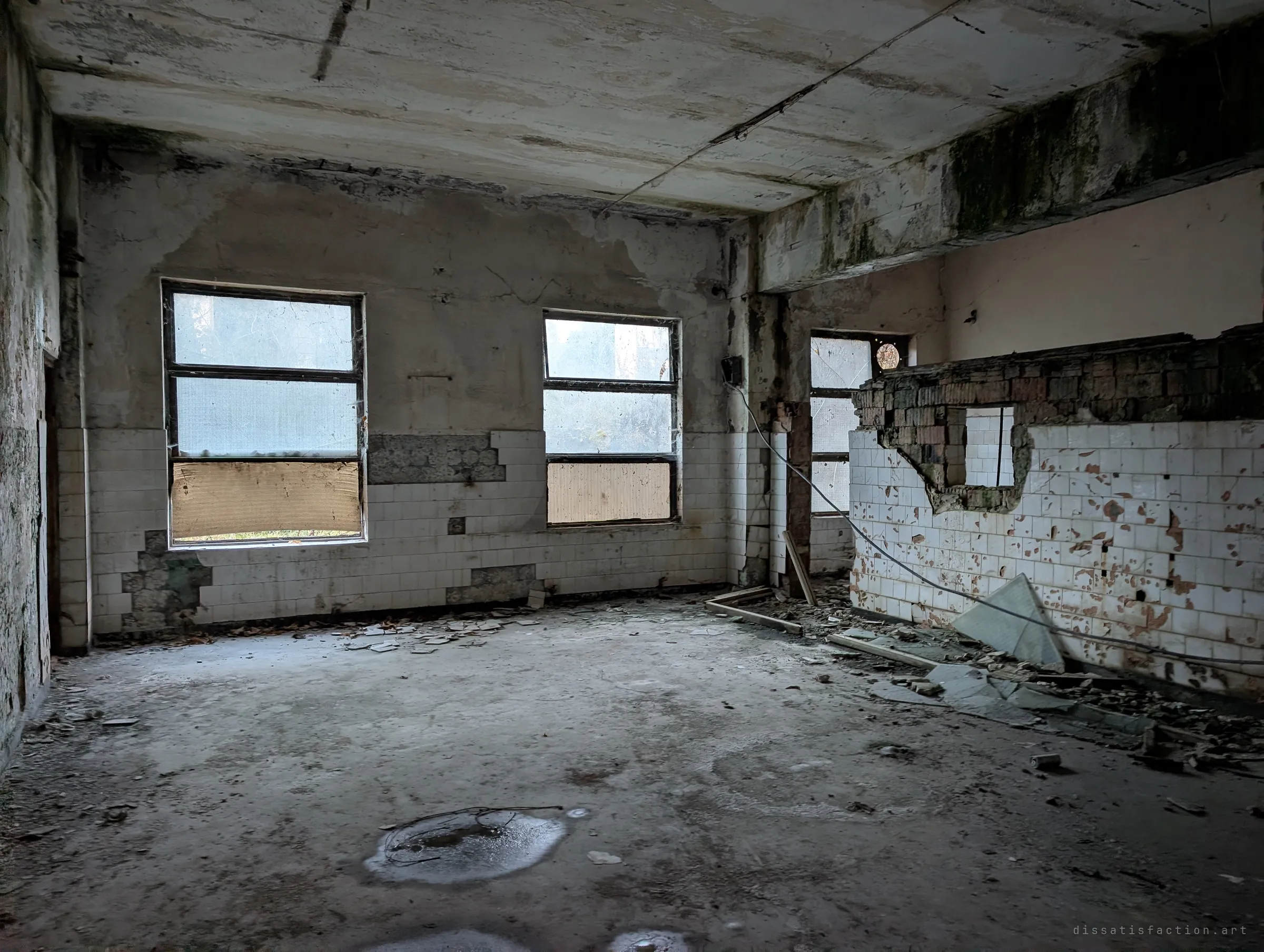 A tiled room with frosted windows and a half-demolished brick partition, cables sagging across a floor of broken tiles.