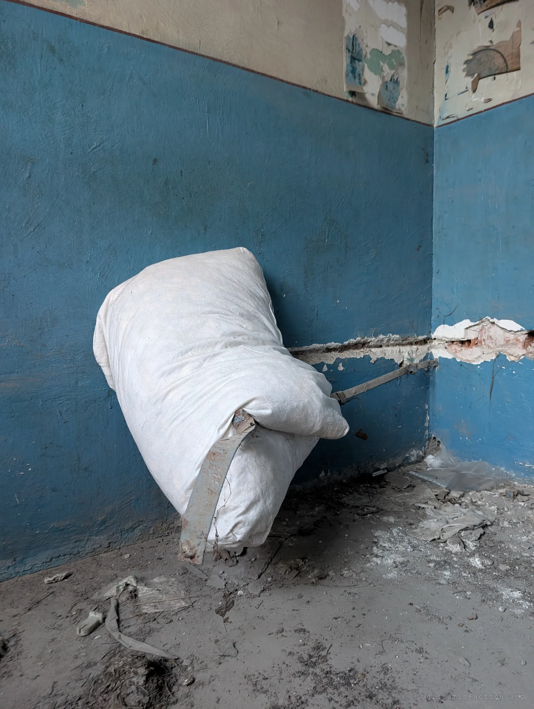 A white sack slumped against a blue-painted wall on a bent metal bracket, a small still life of what was left behind.