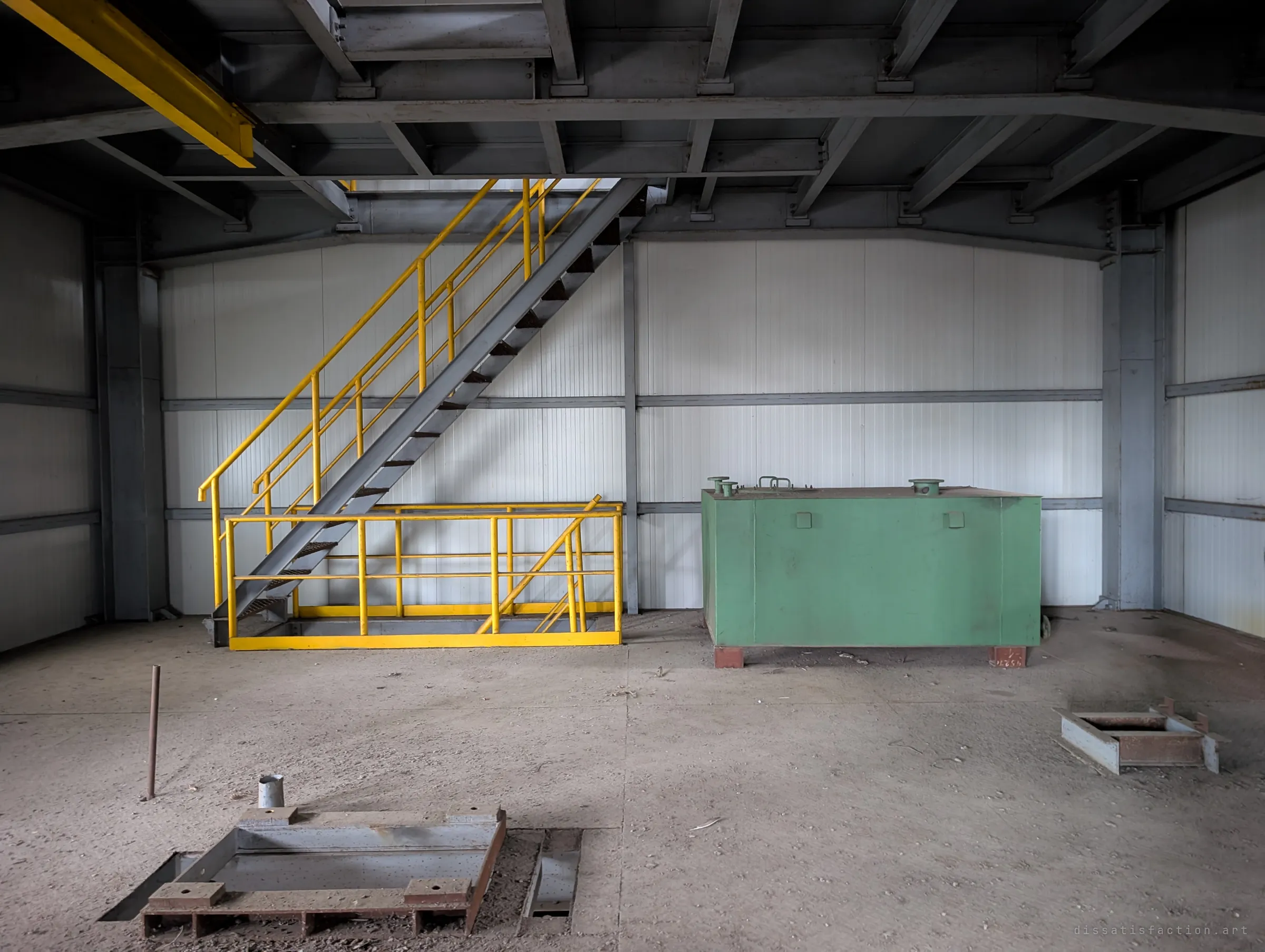 Inside the block, a yellow stair and a green tank stand against clean white panels, with empty mounting frames set in the floor. The room looks barely used before it was left.
