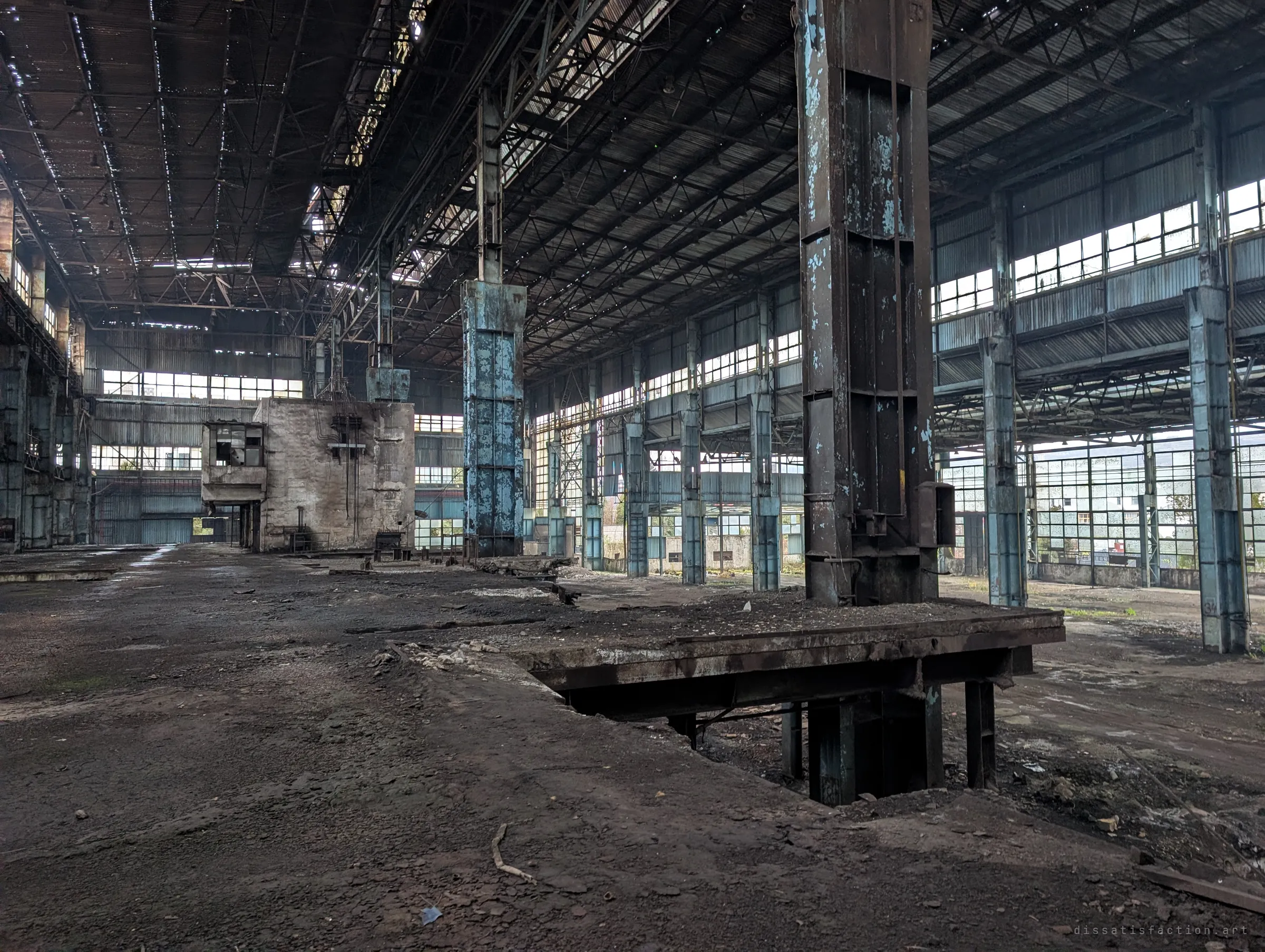 The full length of the hall opens out: a steel machine bed sunk into the floor, a forest of blue columns and walls of grid windows letting in grey daylight.