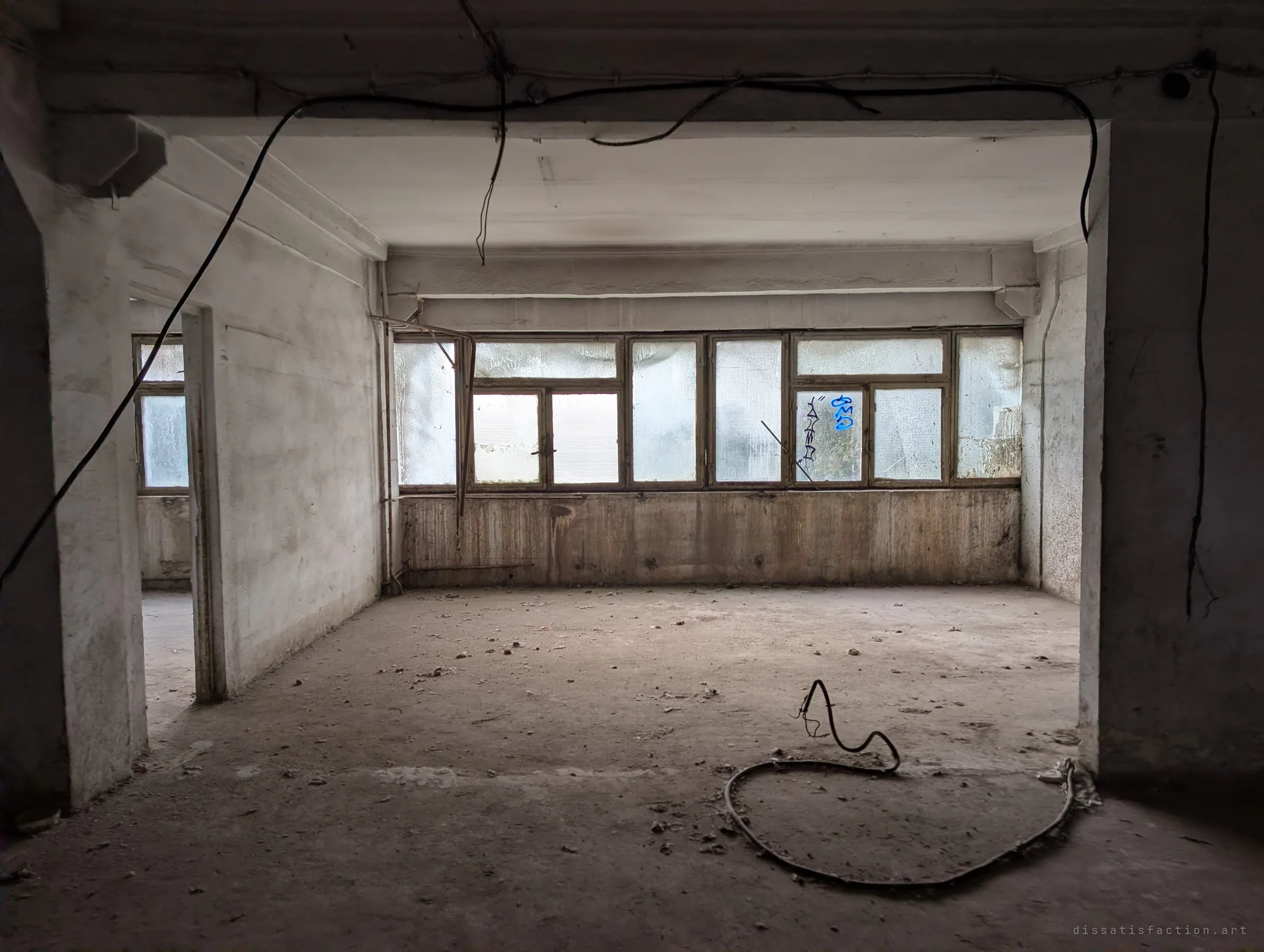 Framed by a wide doorway, a bare office room with a loop of cable on the floor and a band of frosted, tagged windows along the back wall.
