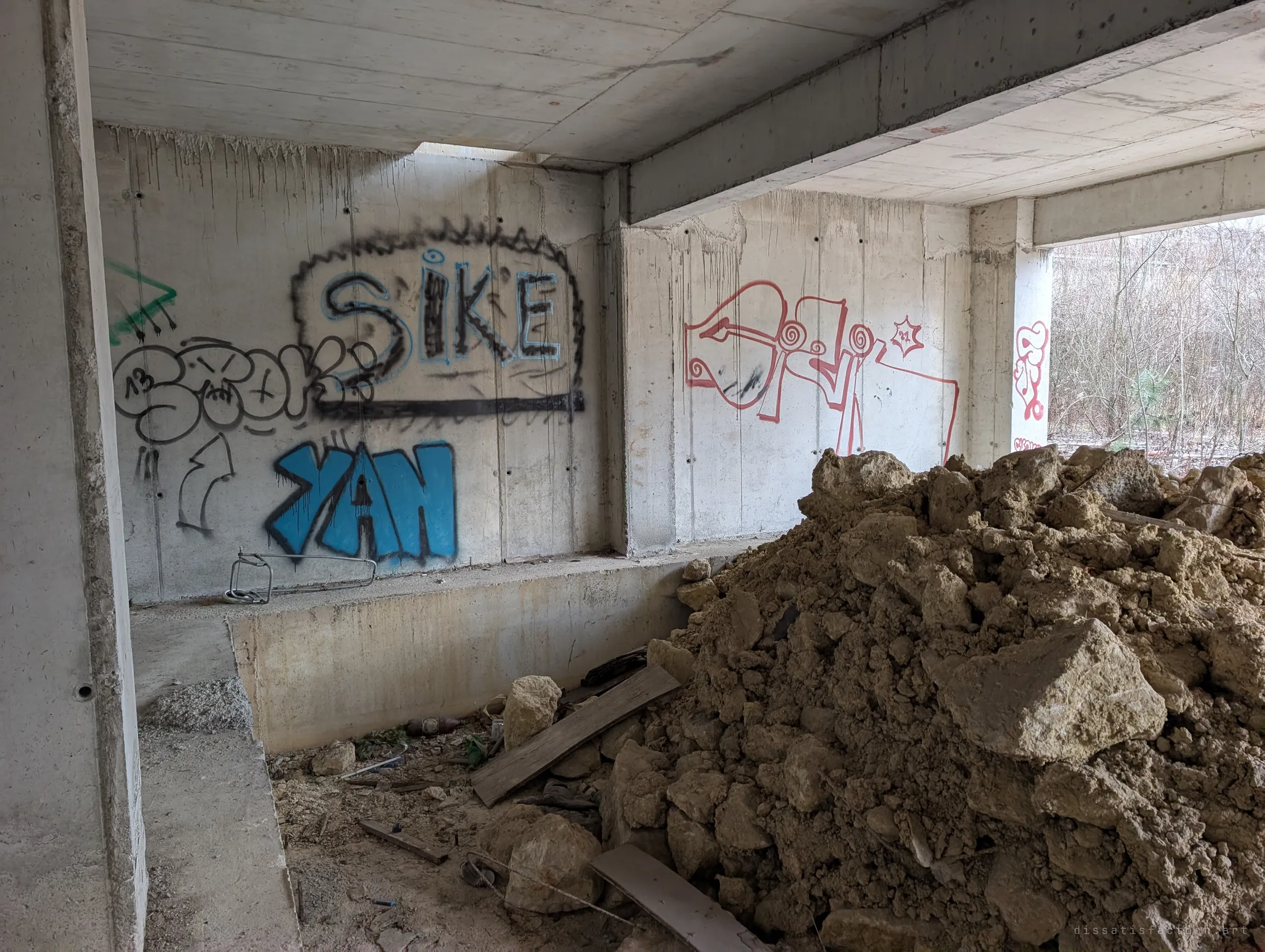 A ground-floor bay with colourful graffiti pieces on the concrete walls and a large mound of dumped earth and rock filling half the room.