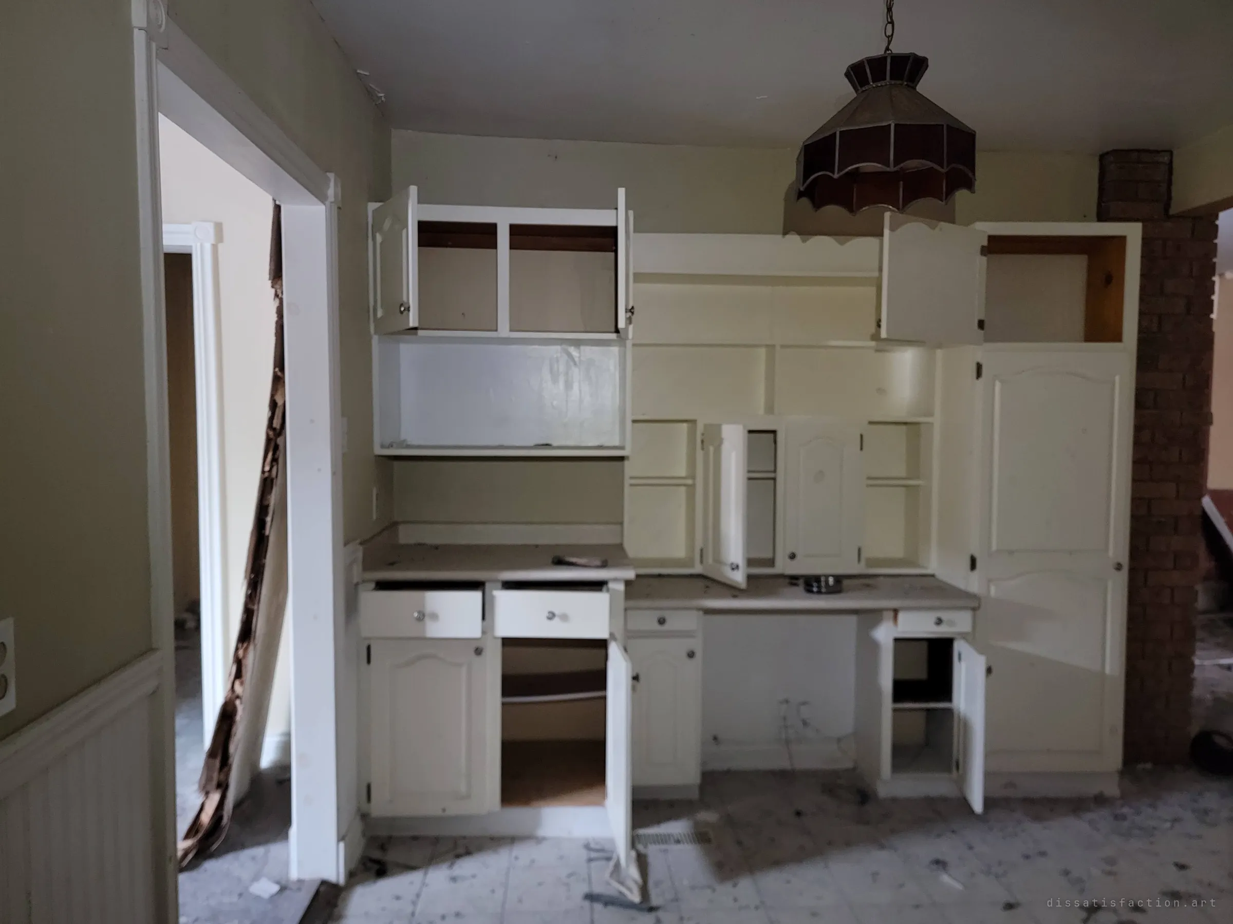 A built-in hutch with its doors hanging open under a stained-glass pendant lamp, a brick column and a doorway to the next room on either side.