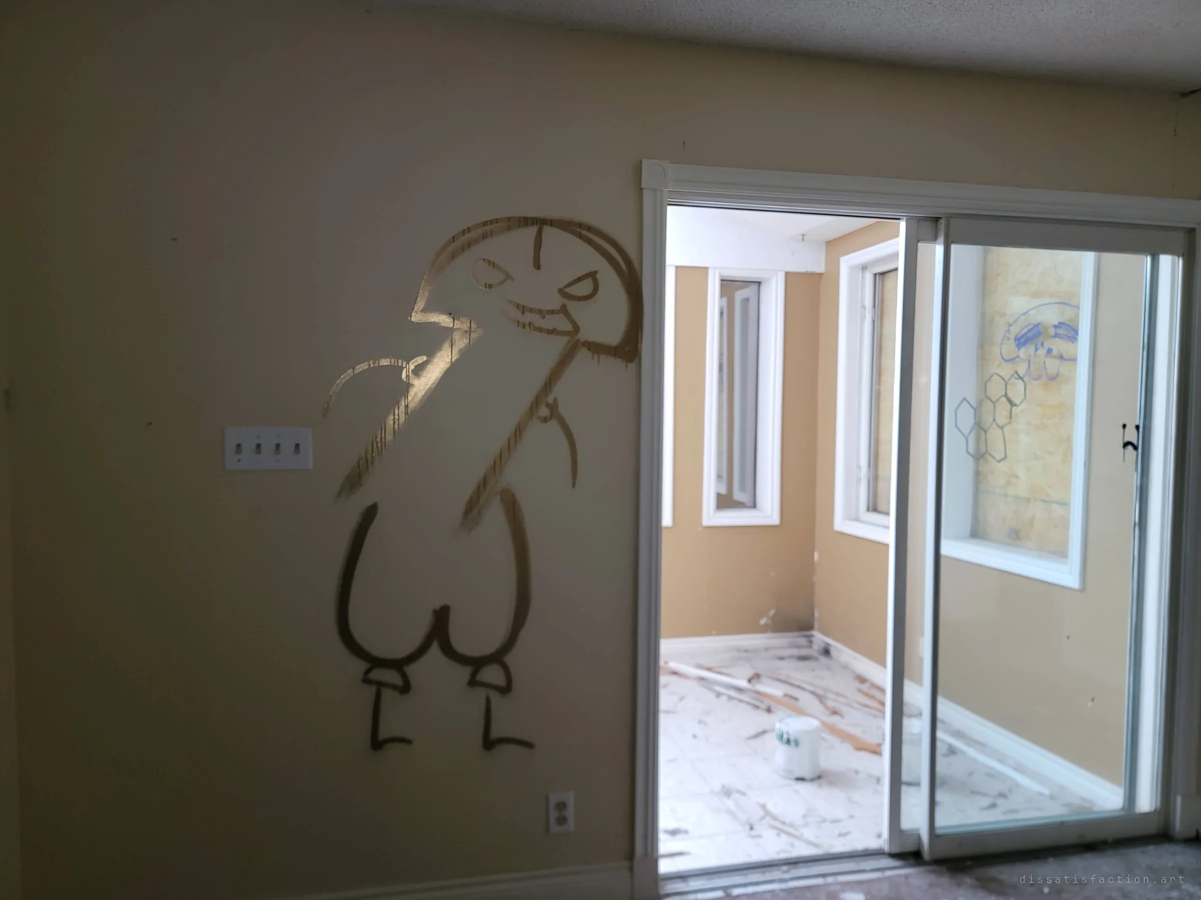 A large gold spray-painted cartoon creature grins beside a light switch, next to a sliding door into a sunroom littered with broken trim and a paint bucket. The boarded window beyond carries more drawings.