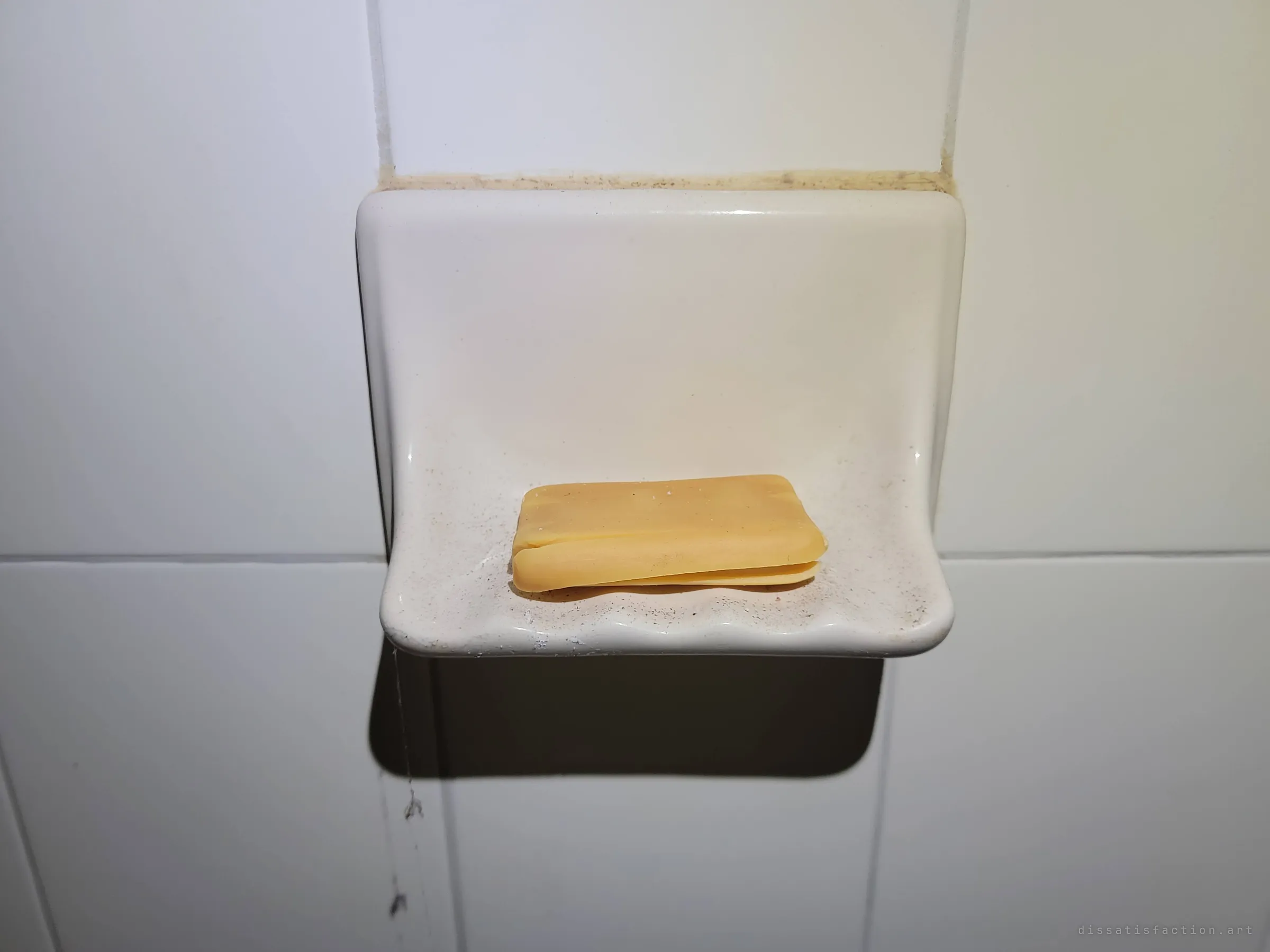 A cracked, dried bar of orange soap still sits in a ceramic soap dish set into white shower tile. A small trace of the people who once lived here.