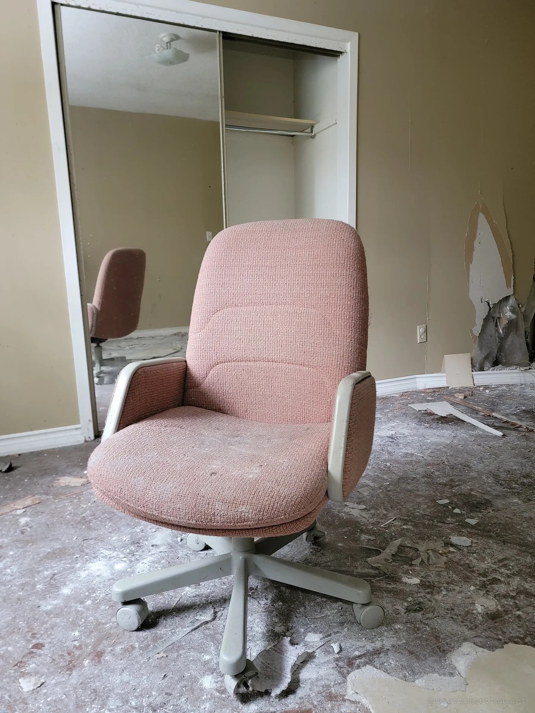 Close on the pink upholstered office chair standing in the debris, its reflection repeated in the closet mirror behind it. Torn drywall exposes insulation on the wall to the right.