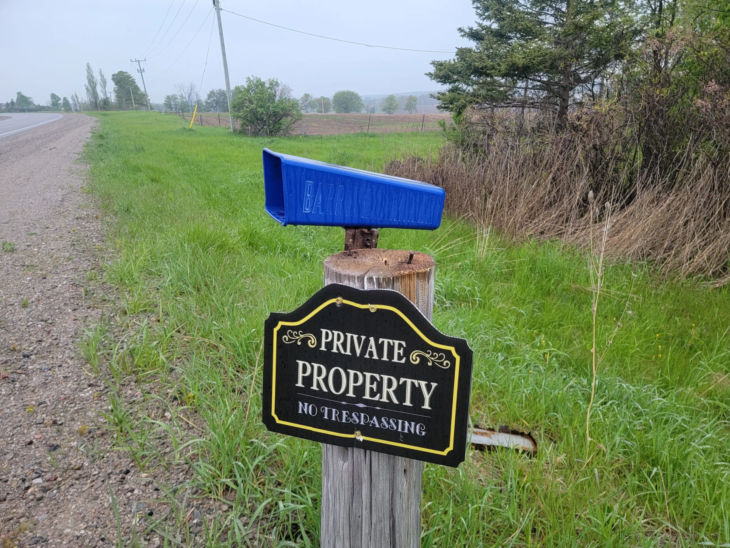 A weathered post at the roadside carries an old newspaper box and a private property sign, the first warning at the edge of a quiet rural road.