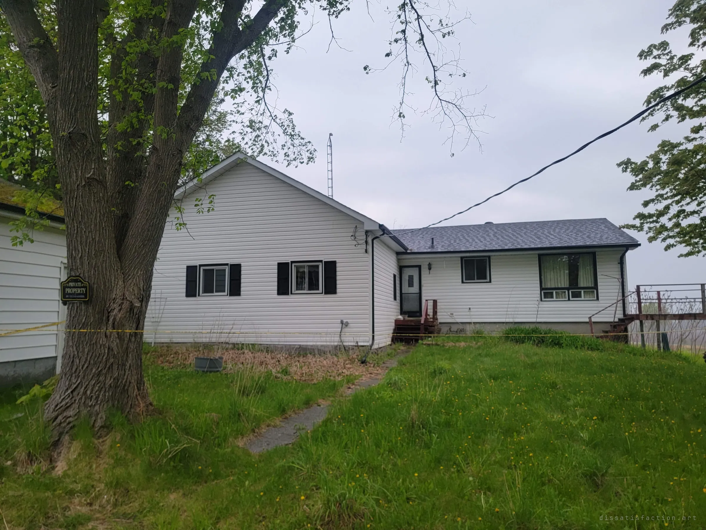 A tidy white bungalow sits behind caution tape and a no-trespassing sign on the big tree out front, its grass left to grow wild.