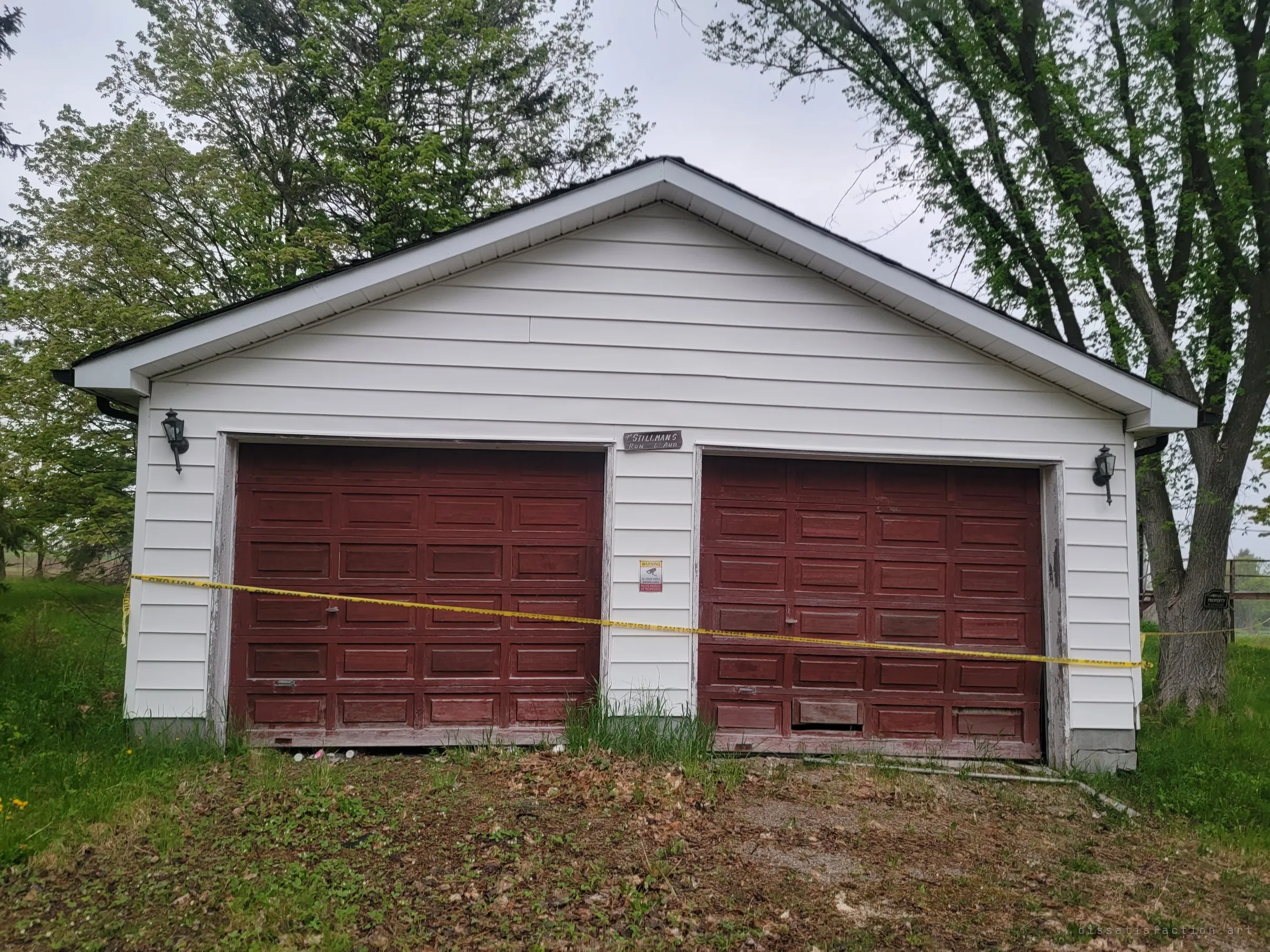 A double garage with faded red doors is strung with caution tape, a surveillance warning posted between the doors.