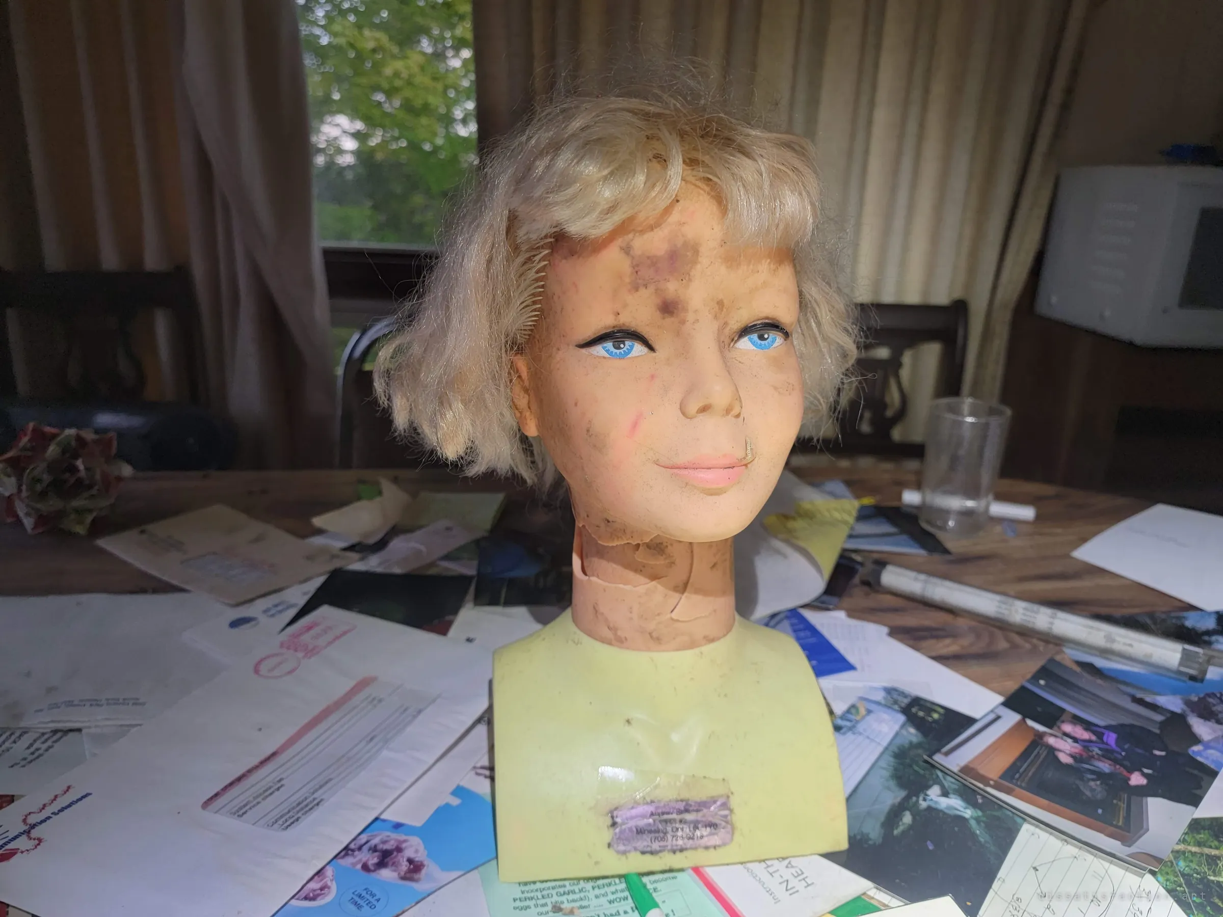 A grimy styling mannequin head smiles over a table buried in mail, flyers and family snapshots.
