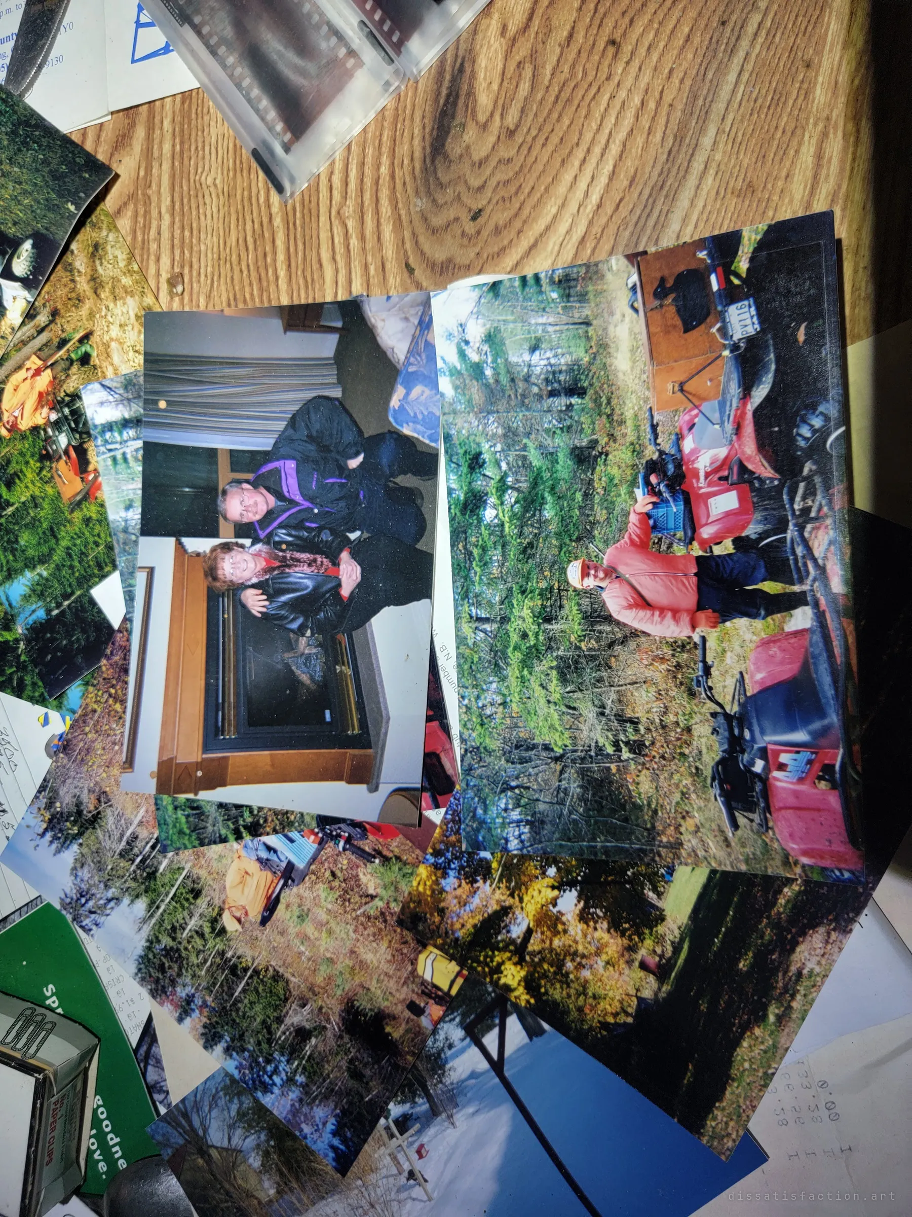 Loose family prints are spread across the table: a couple posing by a fireplace, a man with his ATVs in autumn woods.