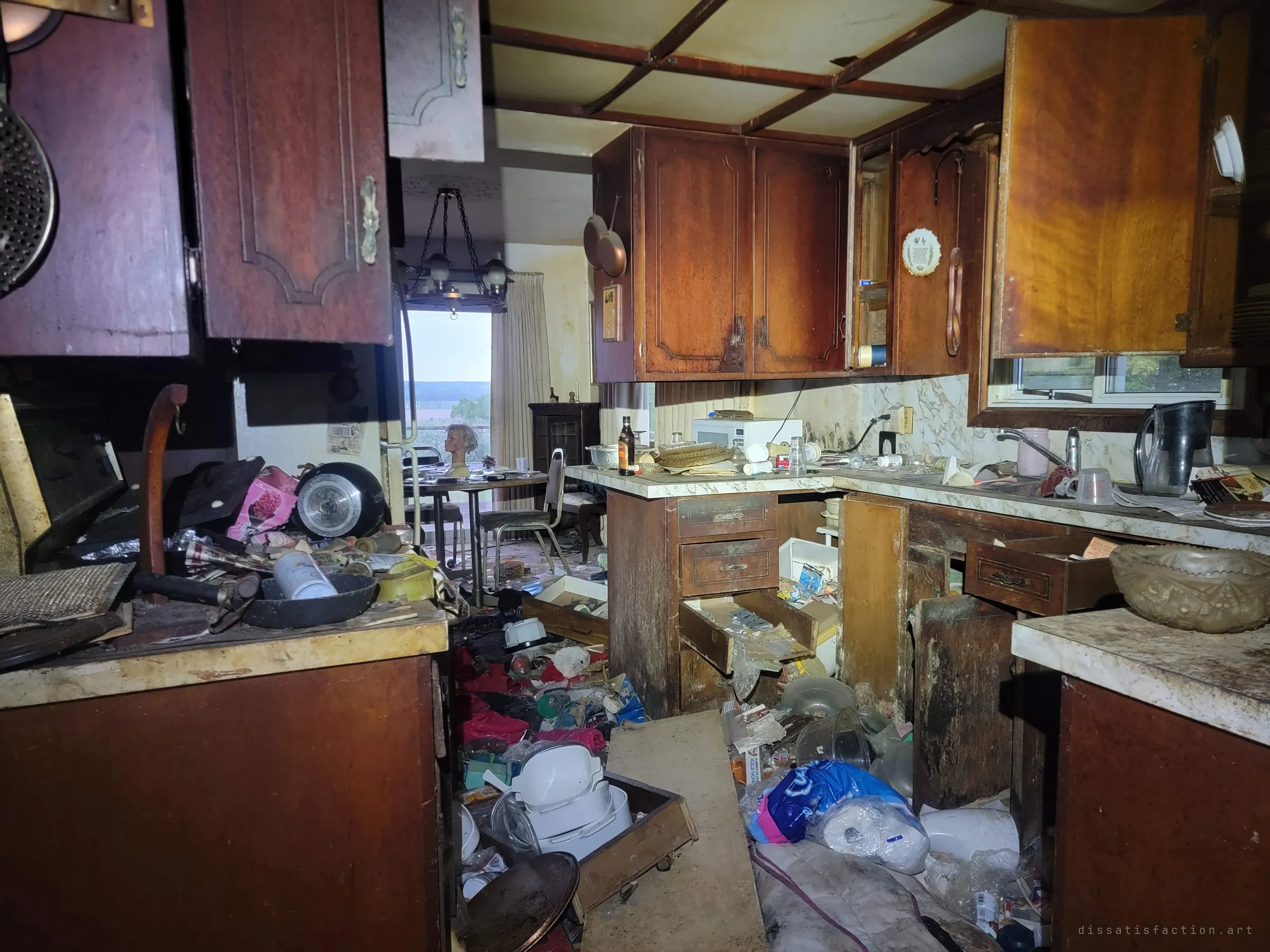 A ransacked kitchen of dark wood cabinets spills its contents onto the floor, with the dining table and mannequin head visible beyond.