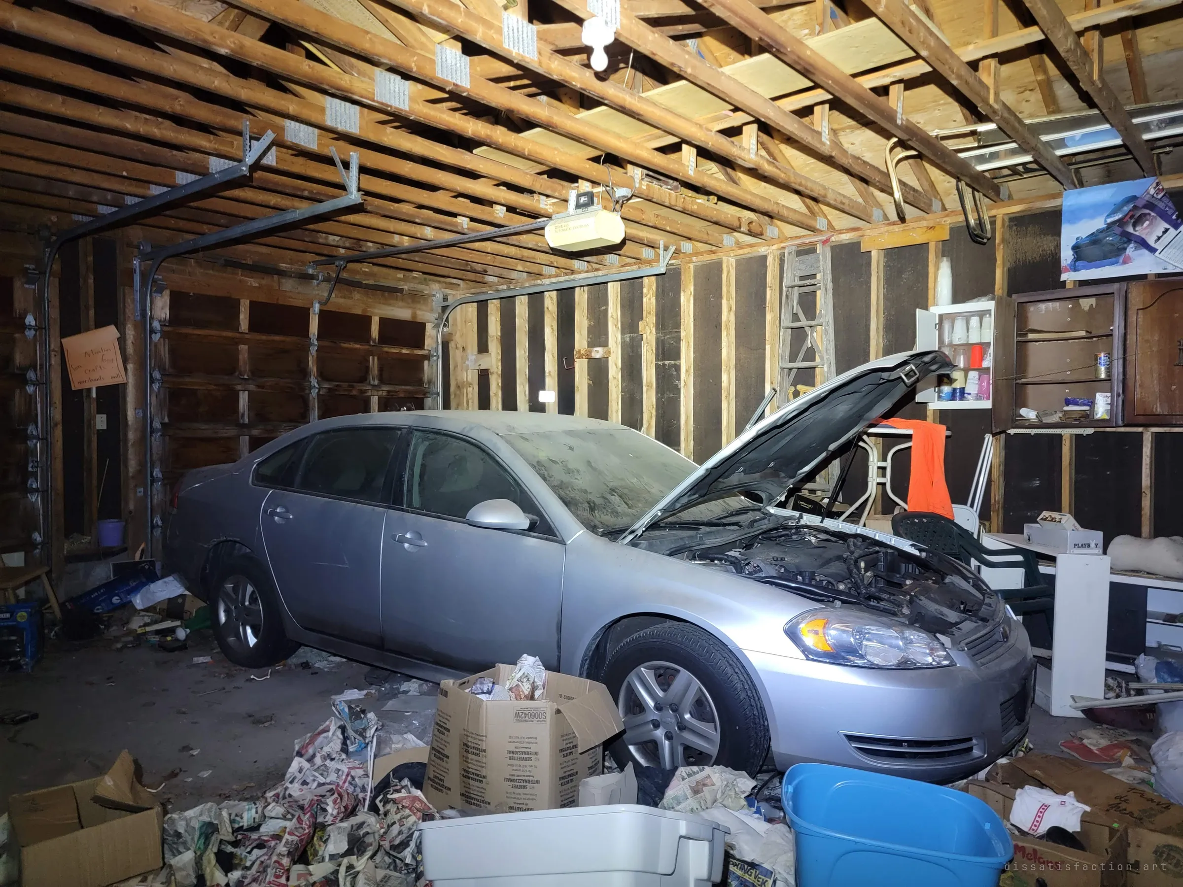 The full two-bay garage, the dust-covered silver sedan nosed in with its hood up among crumpled newspapers, cabinets and a hand-lettered craft-fair sign on the wall. The car anchors the story of a household that simply stopped.