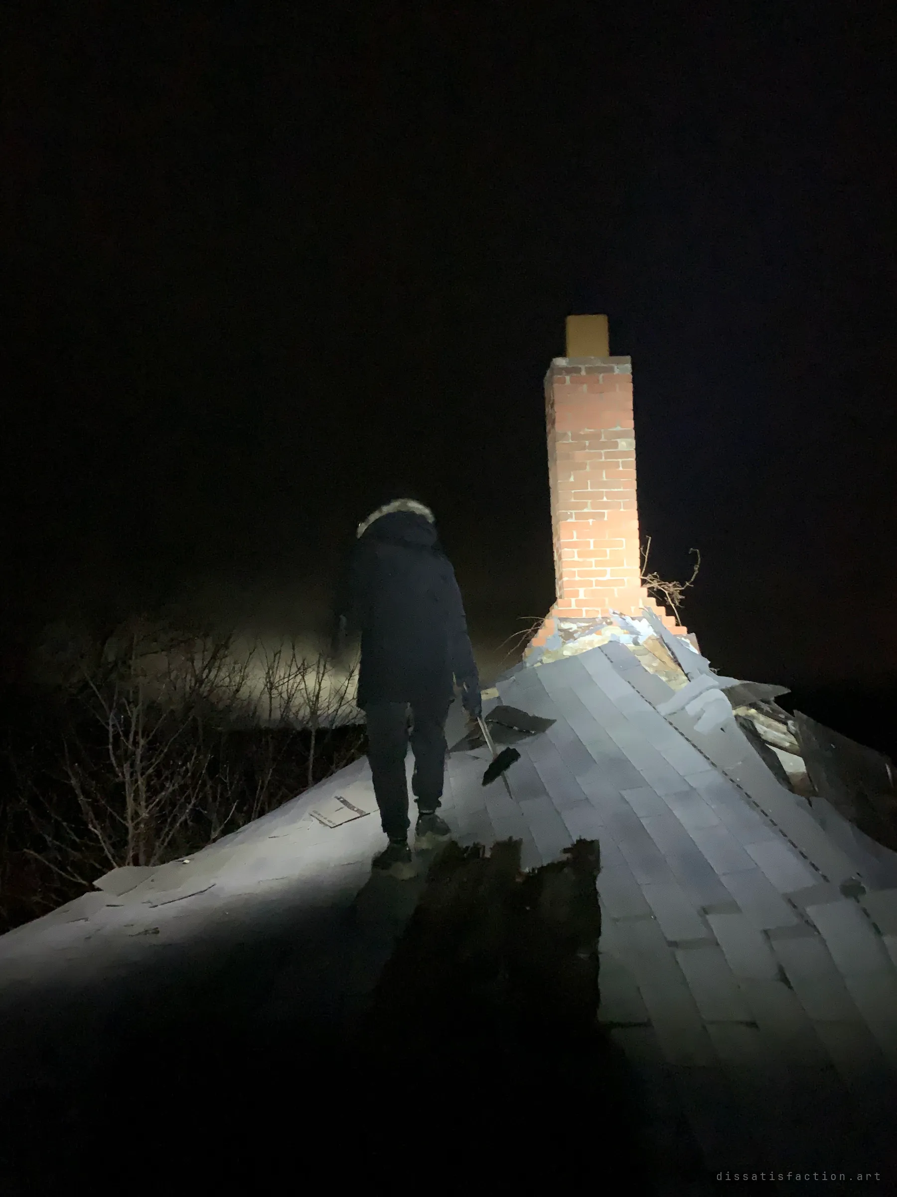 An explorer walks along a collapsing shingled roof towards a lone brick chimney at night. The sagging roofline shows how close the house is to caving in.