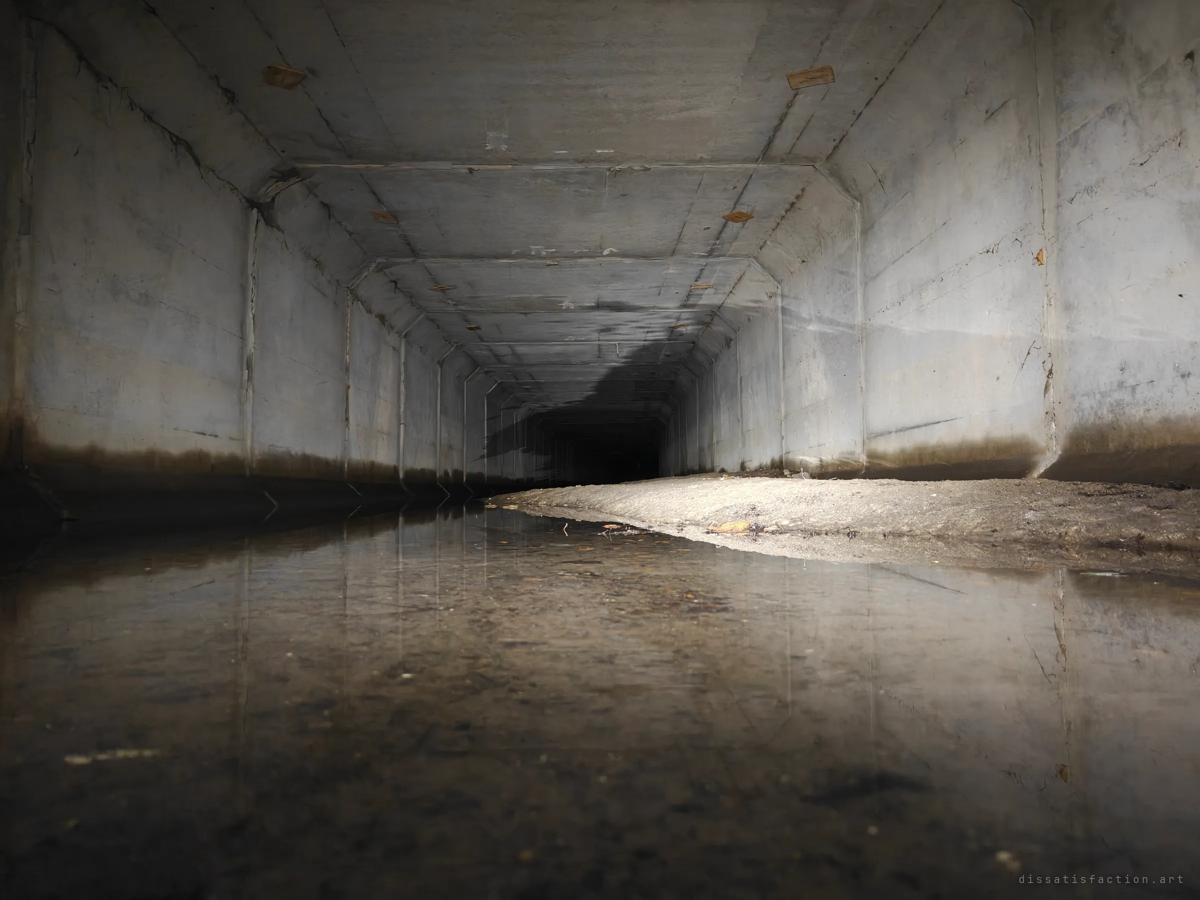 Shot from just above the waterline, the concrete box culvert stretches away to a black vanishing point while a sandy bank of sediment builds up along one wall. The walls and ceiling joints mirror cleanly in the shallow water.