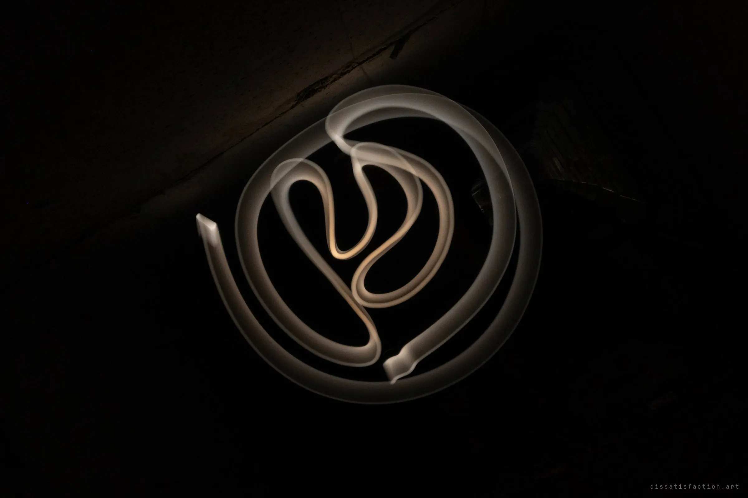 A long exposure light painting: a pale ribbon of light loops into a spiral and a looping knot in the middle of the dark tunnel. A crack along the concrete ceiling is just visible at the top left.