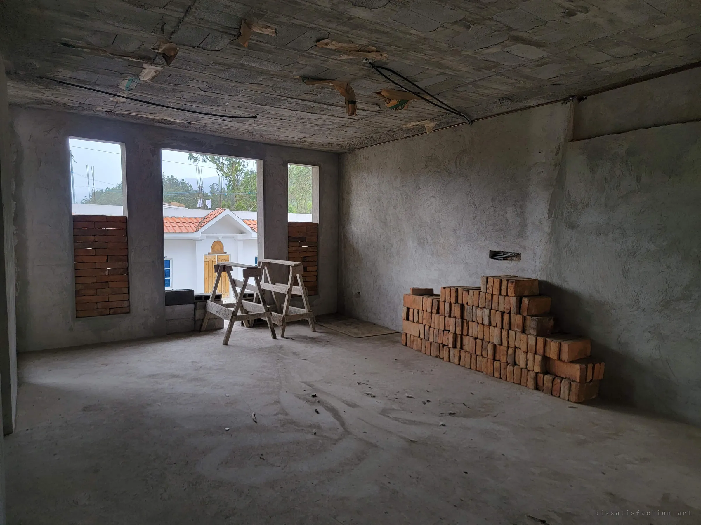 An empty upstairs room with a rough block ceiling, sawhorses in front of half-bricked windows and a neat stack of orange bricks against the wall. The job was left mid-task.