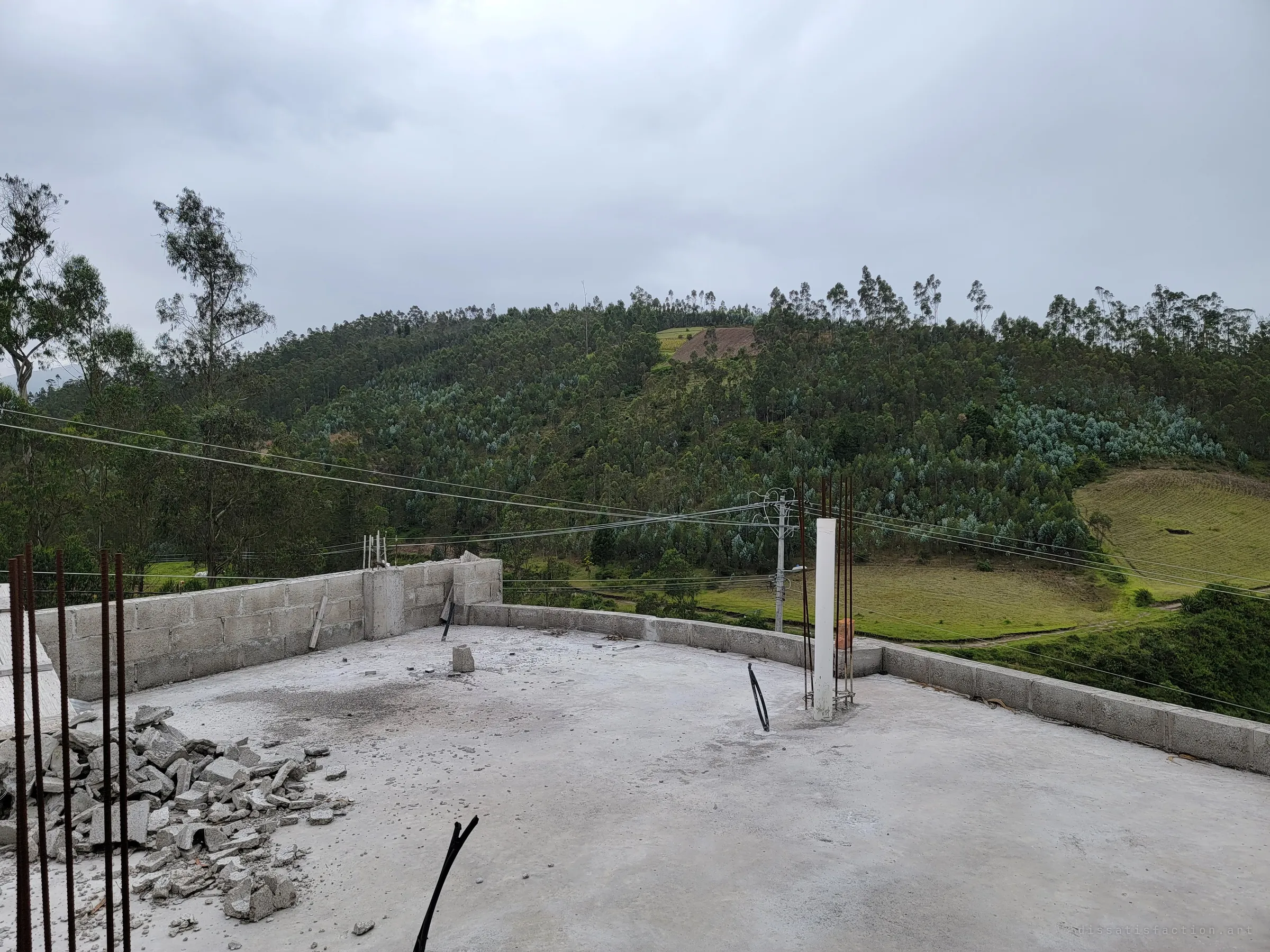 The flat concrete roof stretches toward a eucalyptus-covered hill, with rebar sprouting from unfinished columns and rubble heaped in the corner. The next storey was planned but never built.