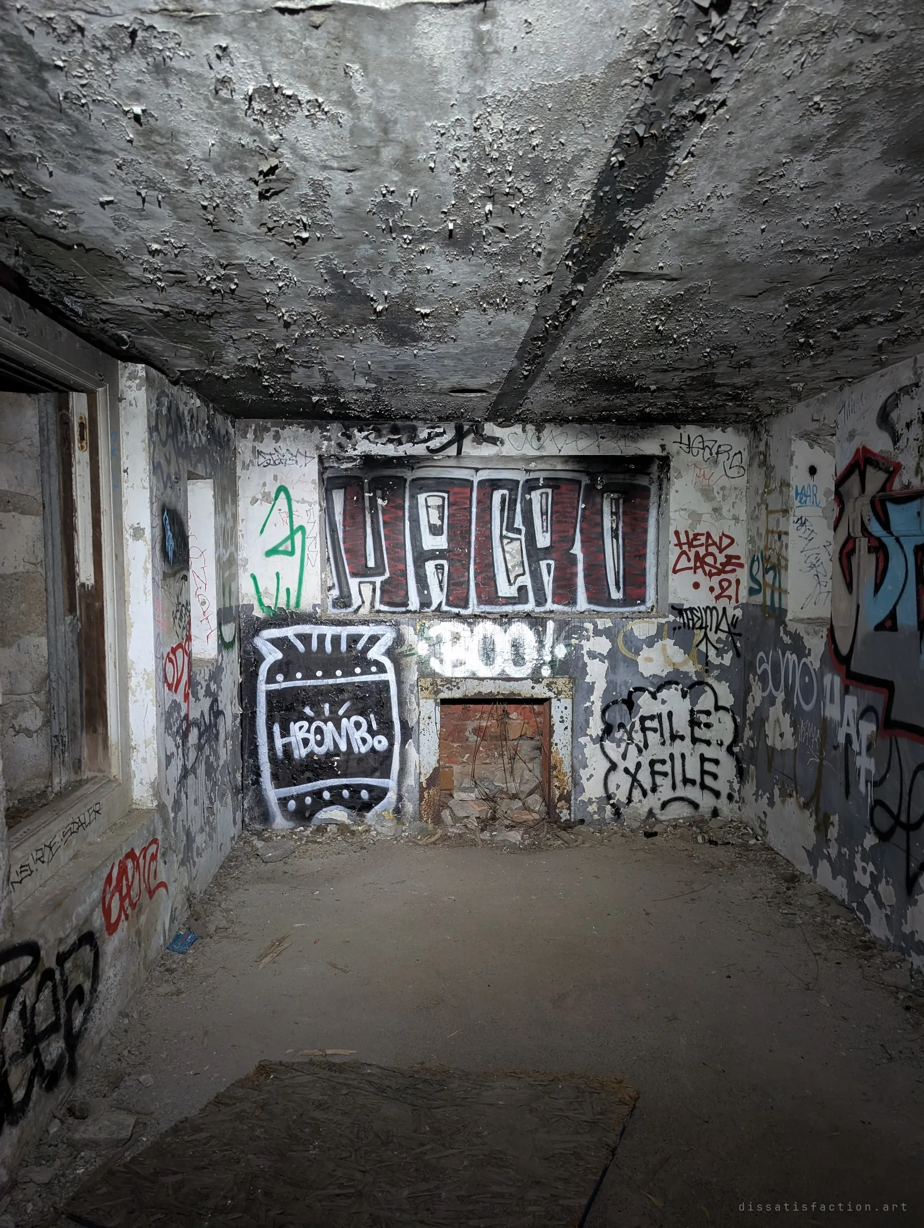 A low concrete room with a blistered ceiling and walls covered in large graffiti pieces around a bricked-up opening. The space has become a gallery for local writers.