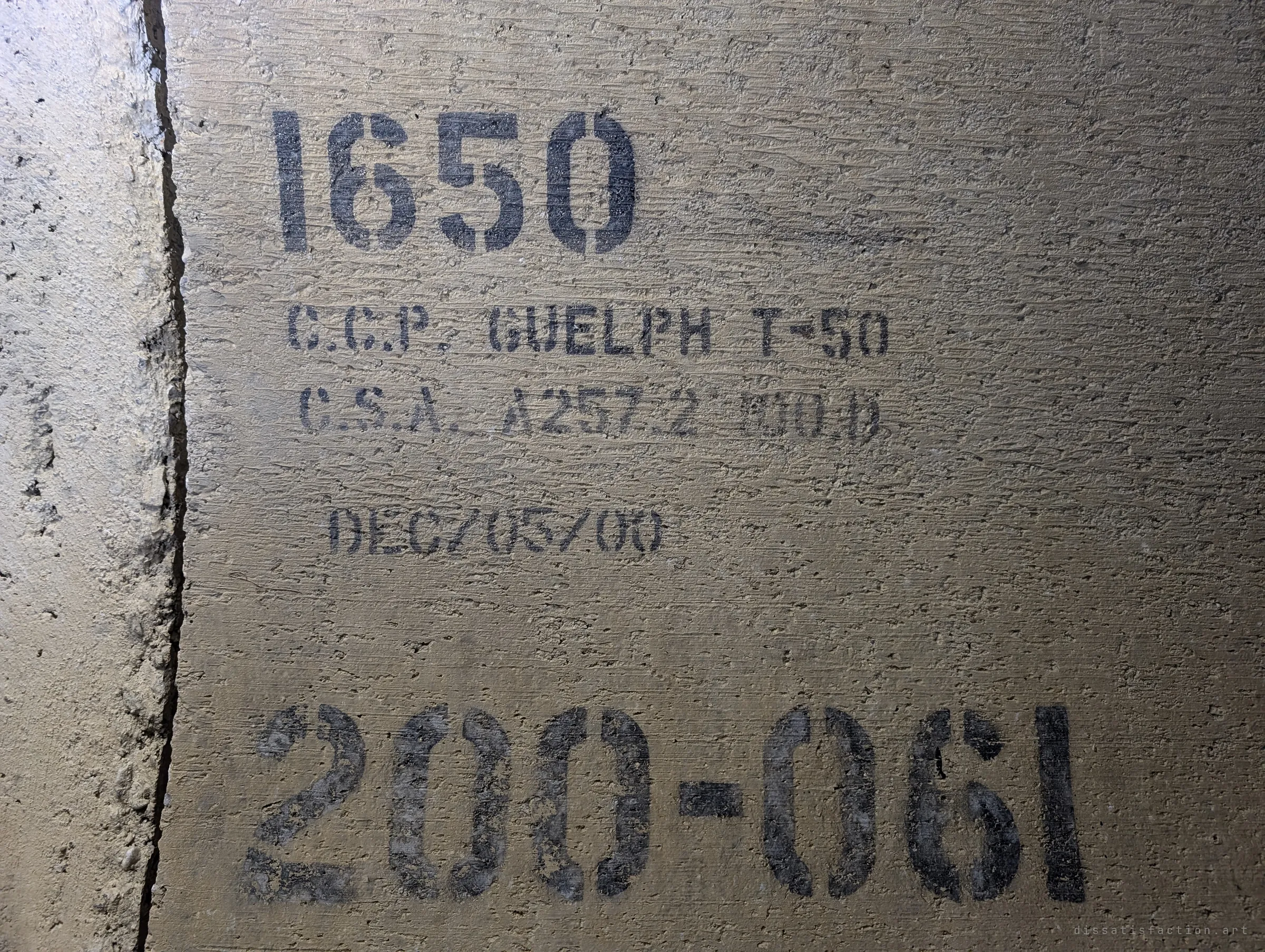 Another size stencil and a late-2000 casting date, with a big stencilled section number underneath, on the pipe wall in warm flashlight.