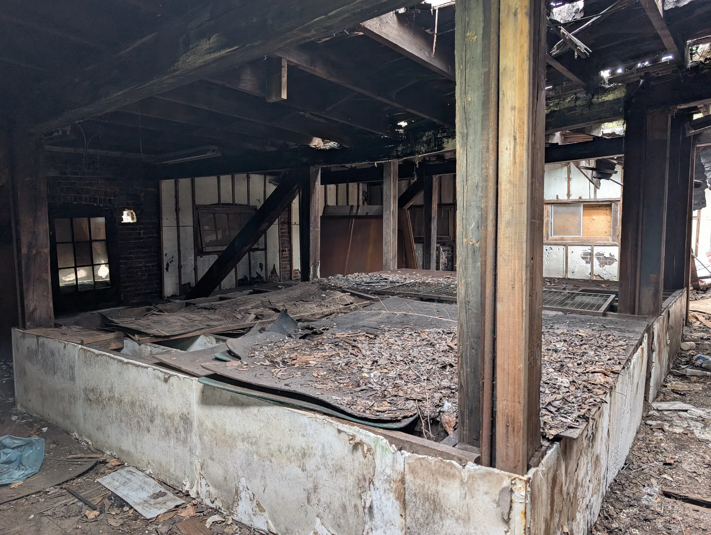 Heavy timber posts rise from a raised planting bed buried in dead leaves and rotting boards, under a sagging, partly open roof. It looks like the old growing area left to rot.