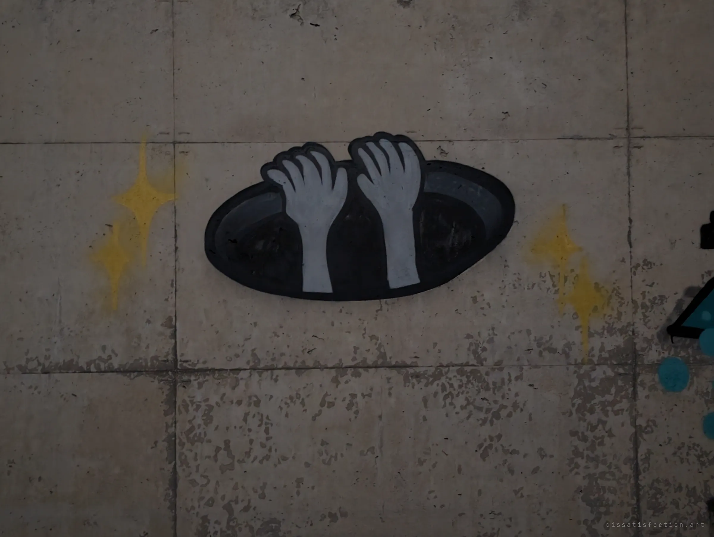 Two pale hands reach up out of a painted black hole, flanked by yellow sparkles. A simple, eerie trompe-l'oeil on the worn concrete.