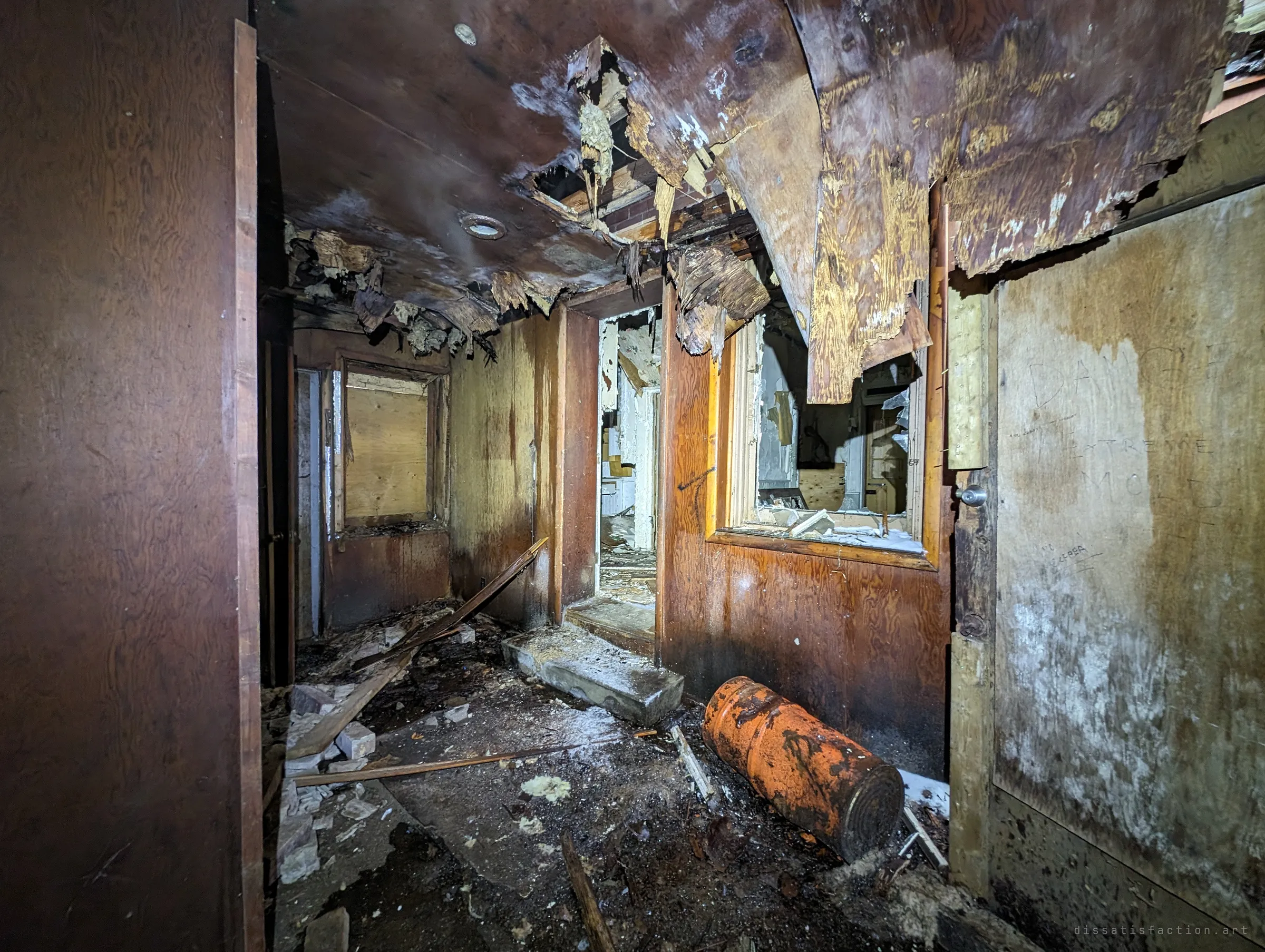 A dark wood-panelled hallway with the ceiling veneer peeling down in sheets and a rusted orange tank lying on the floor. A mold warning is scratched into the wall on the right.