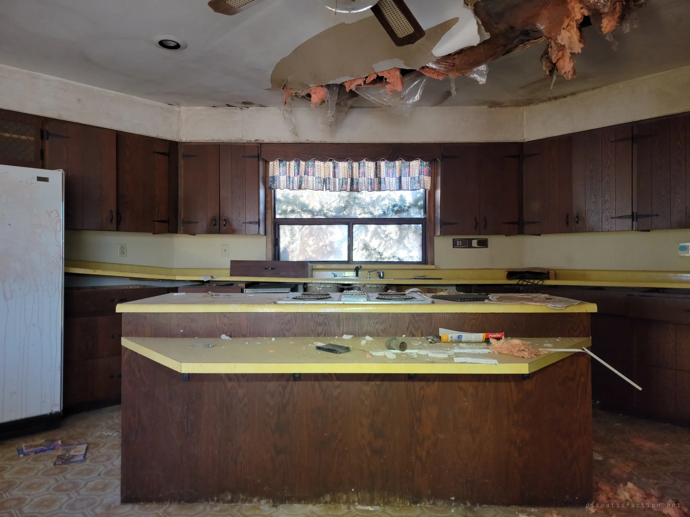 Straight on to the kitchen island and the window over the sink, where a collapsed ceiling spills pink insulation above yellow countertops.