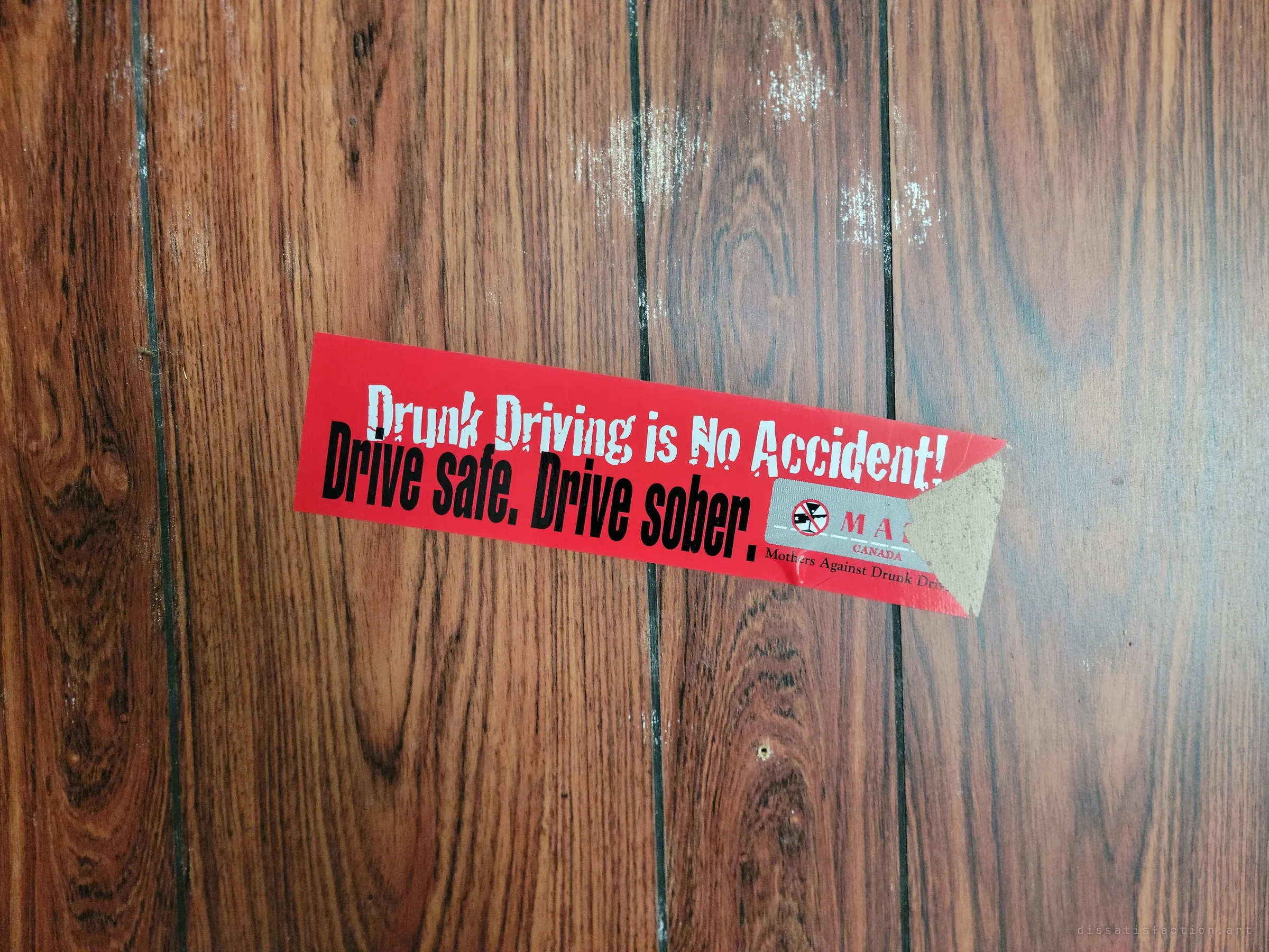 A torn red anti-drunk-driving bumper sticker stuck crooked on dark wood panelling. A leftover slogan from another decade.